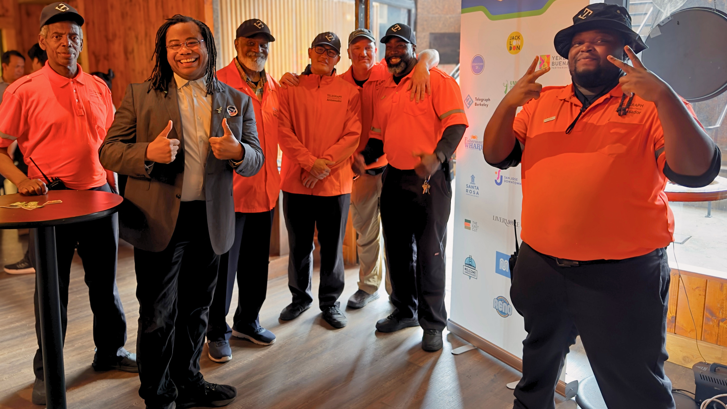 Aidan Hill stands smiling with Telegraph Ambassadors in orange uniforms at the TBID annual meeting.