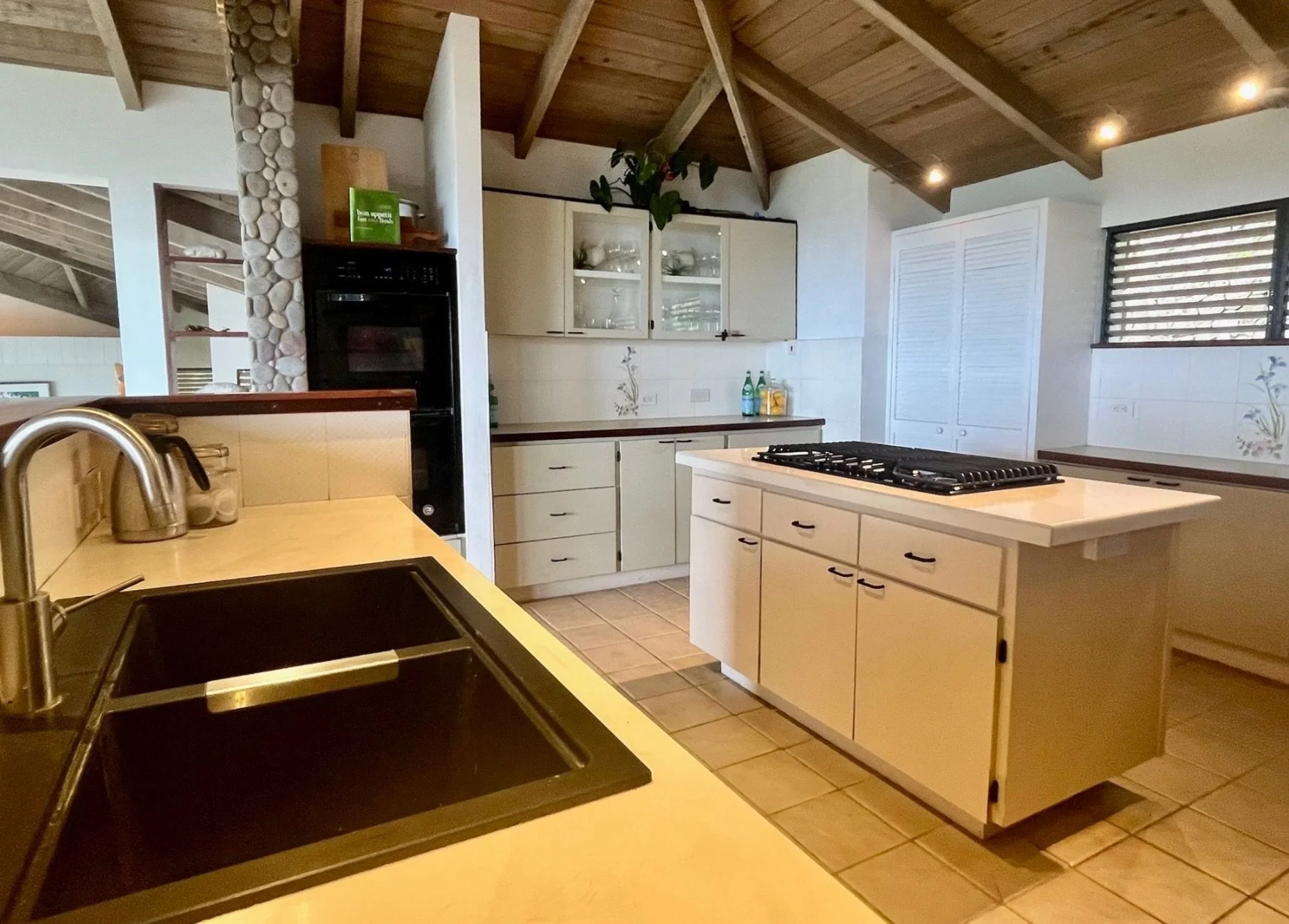 Kitchen with a black sink, beige countertops, a stove on an island, cabinets, a window with horizontal blinds, and a wooden ceiling.