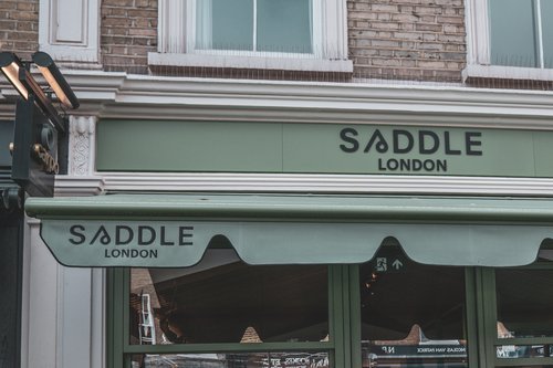 Storefront with green awning displaying the text 'SADDLE LONDON' in black lettering.