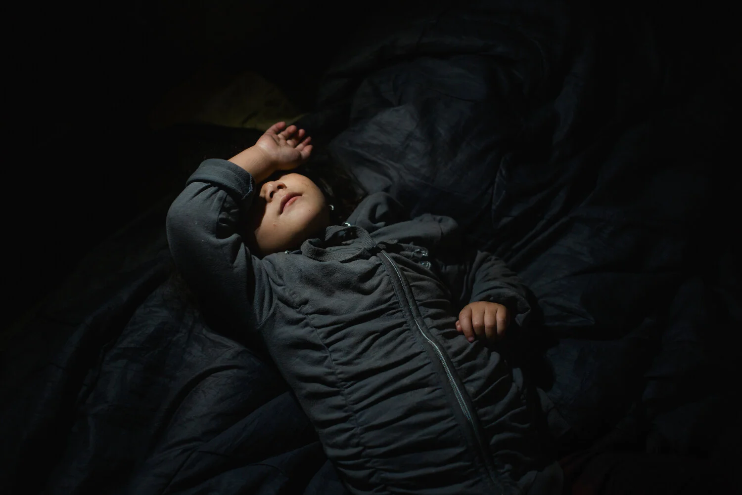  Moria Camp, Lesbos - 29/11/2019  Safar (age 6) on a sleeping bag at night, moments before she falls asleep. Two small pop-up tents joined together with a tarp serve as a home for the young Afghan girl and her family, who are staying in the Moria cam
