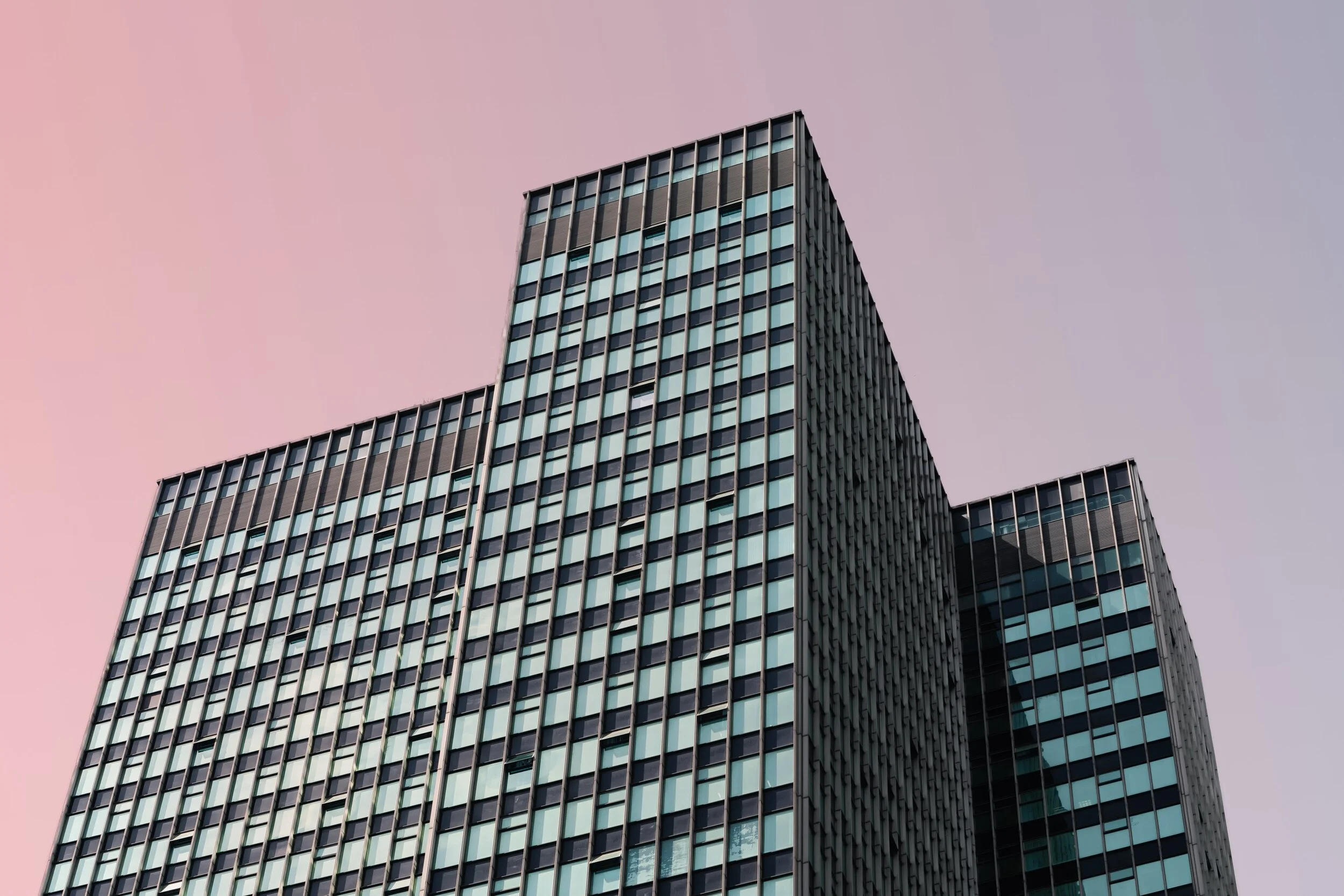 Tall modern glass office buildings against a pastel pink and purple sky.