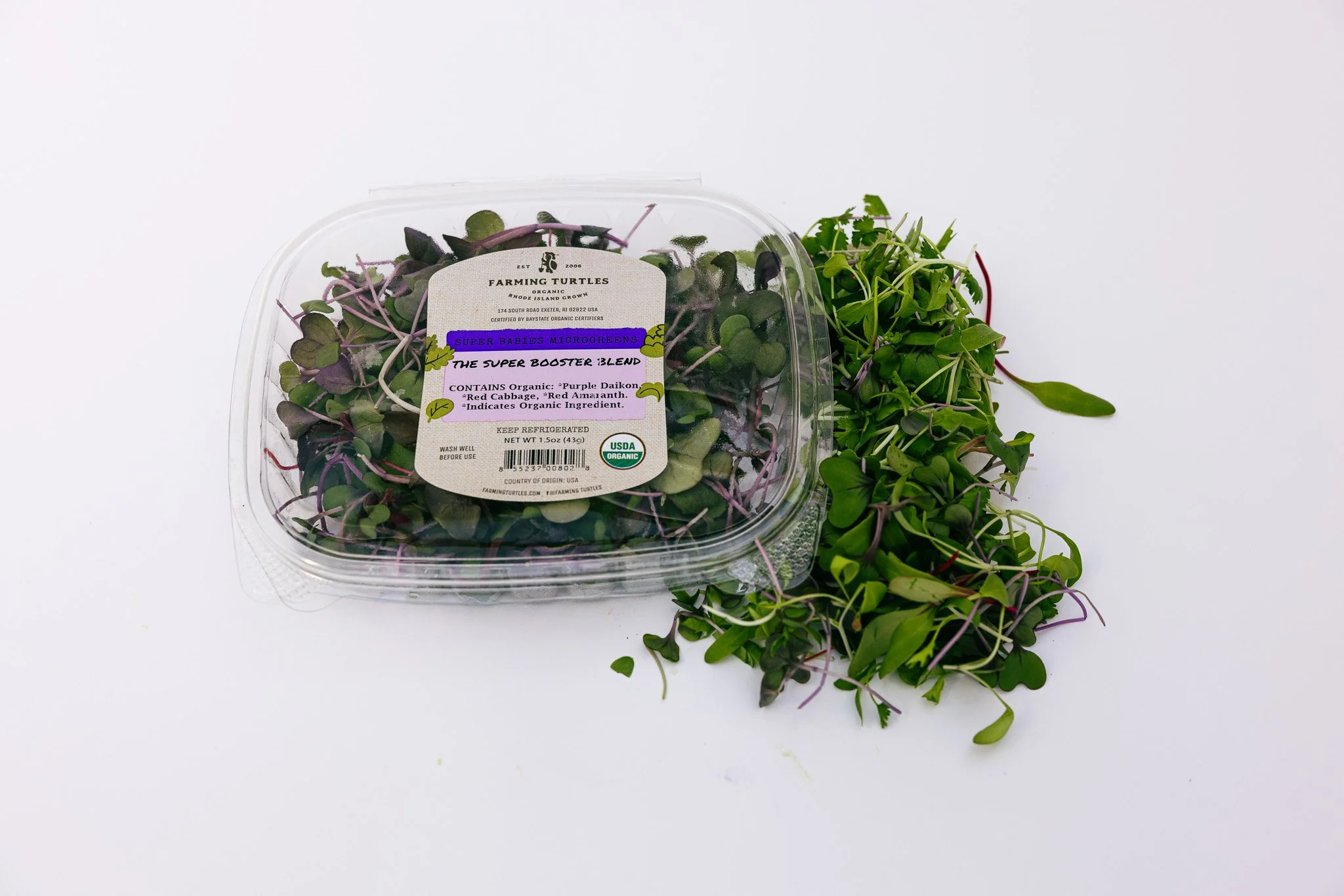 Container of microgreens labeled 'Super Babies Microgreens' placed on a white surface with some microgreens spilled outside the container.
