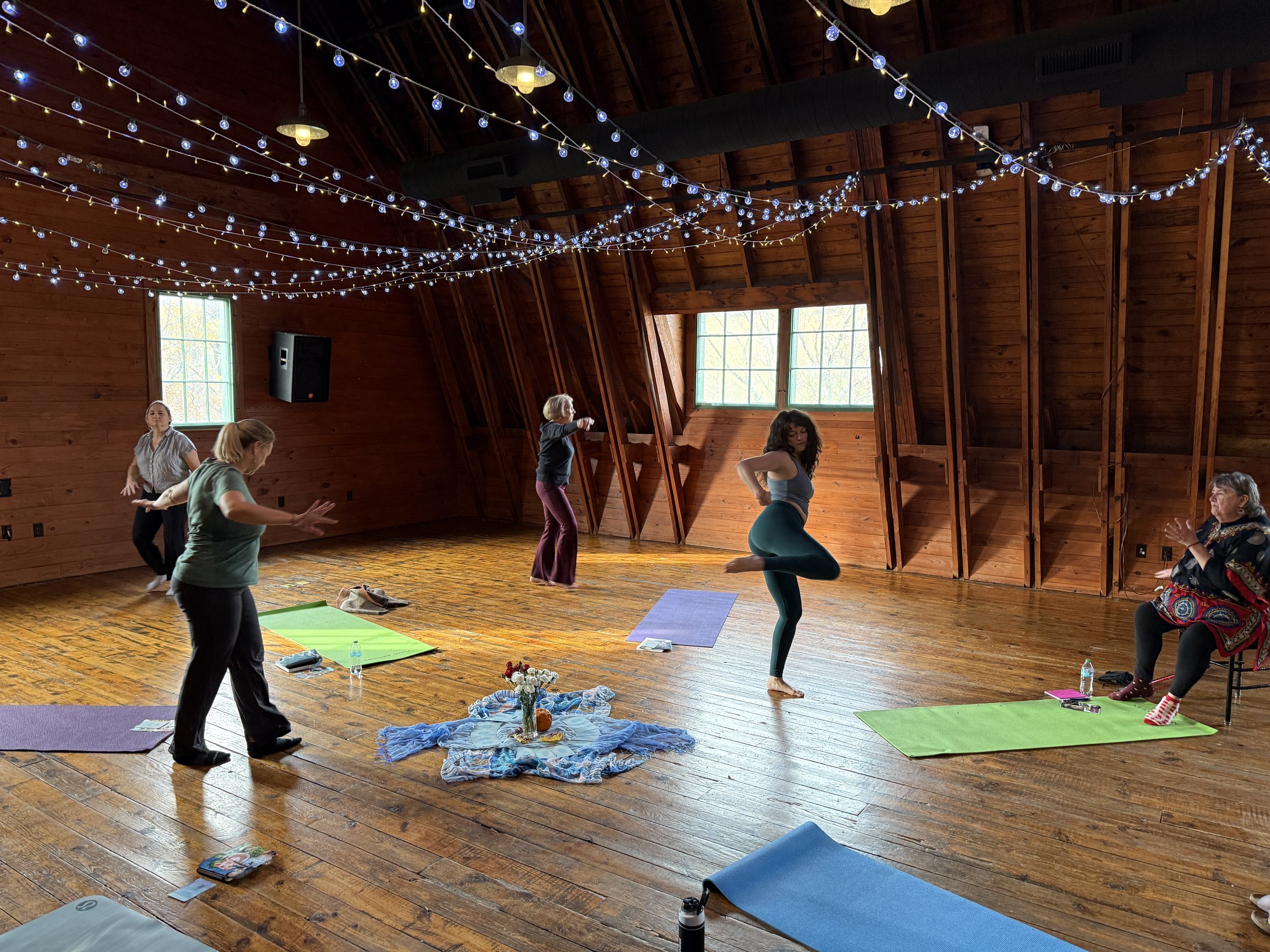 Women dancing freely with yoga mats, wood floors, and hanging lights.