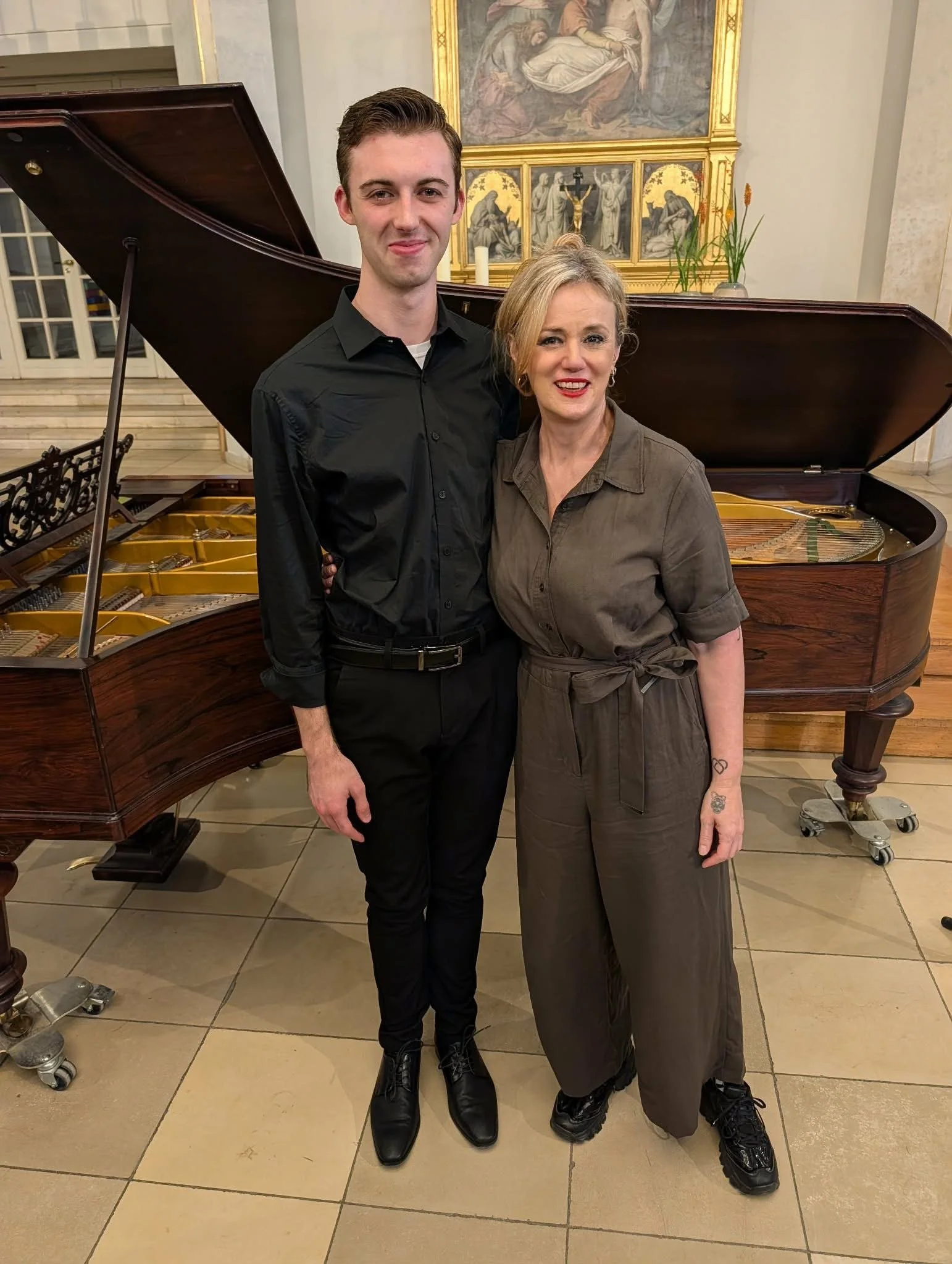 Pianist DJ Cleavinger and Mezzo-Soprano Aleise Bright standing in front of piano both smiling
