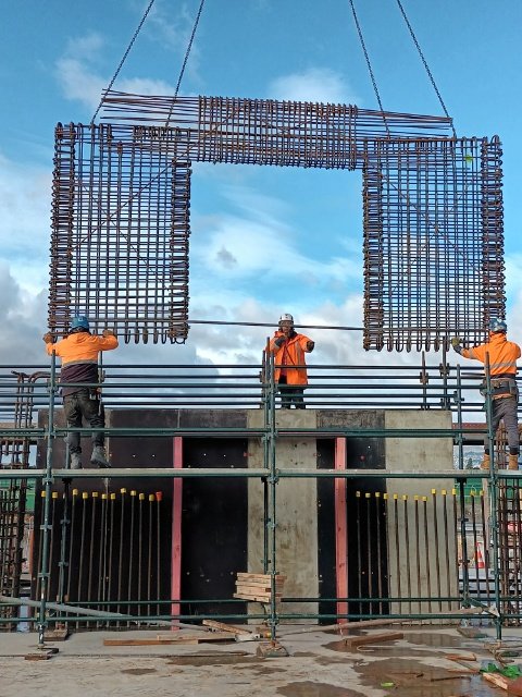 three steel fixers guiding steel frame on a crane into place