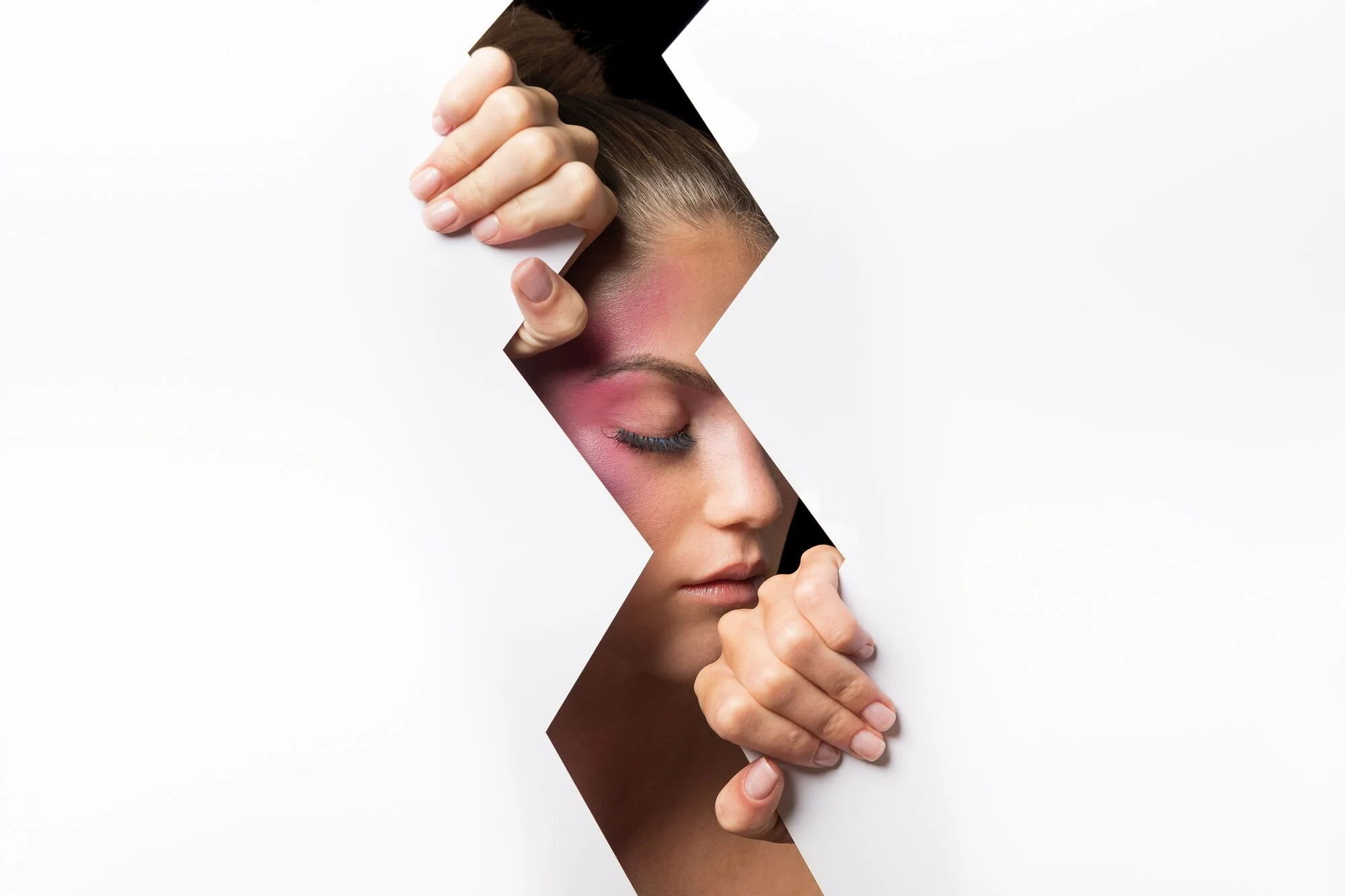 Frau mit buntem Make-up, die durch eine zerbrochene weiße Wand schaut.