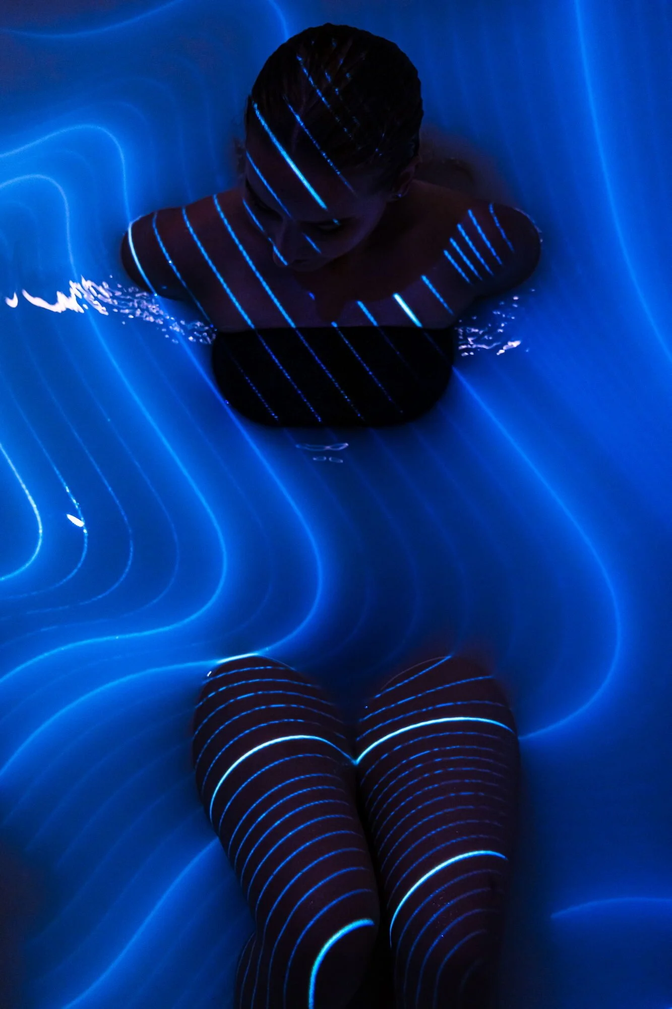 Eine Person sitzt in einem dunklen Raum mit blauen Leuchlinien, die ihren Körper und die Umgebung beleuchten.