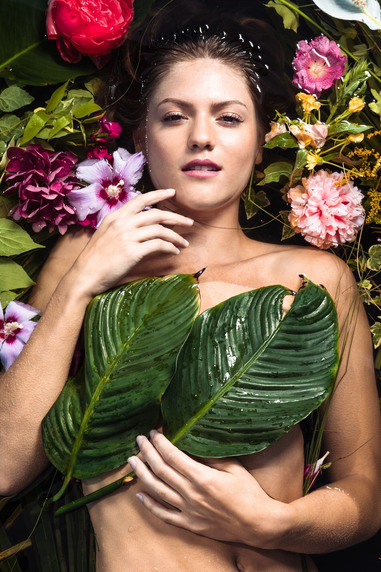Junge Frau mit nassem Haar umgeben von bunten Blumen und großen grünen Blättern