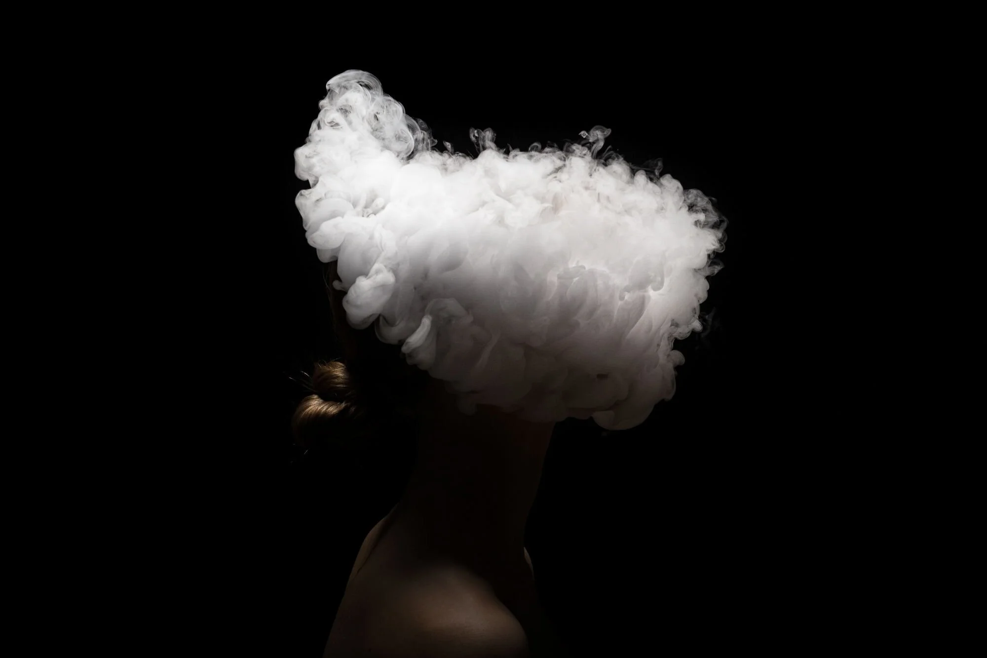 Eine menschliche Silhouette mit einem großen Rauch- oder Dampfwolkenkopf, vor schwarzem Hintergrund.