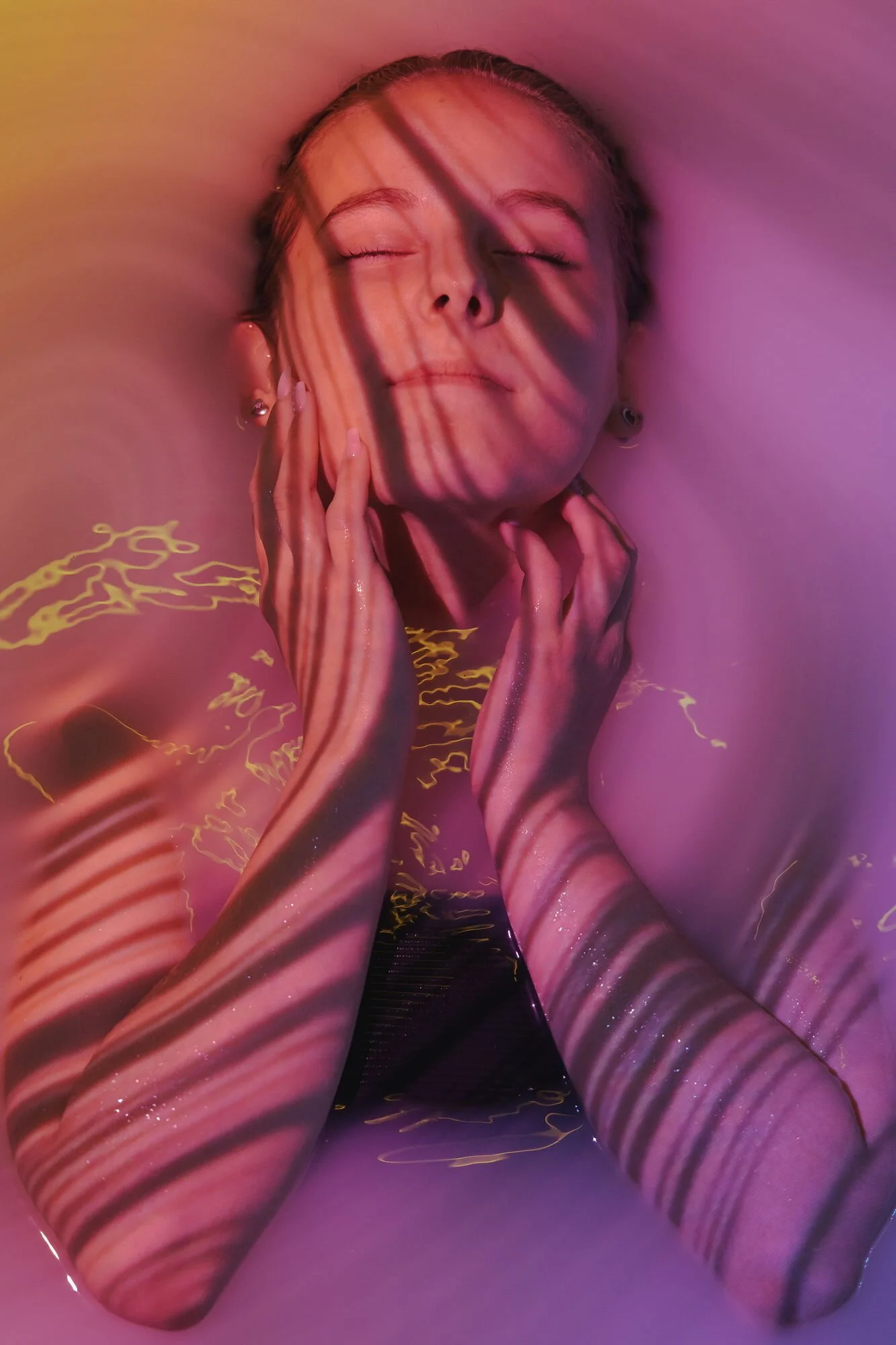 Eine junge Frau mit geschlossenen Augen entspannt, während sie in einem Bad mit schimmerndem Wasser ist, das von buntem Licht und Schattenmuster beleuchtet wird.