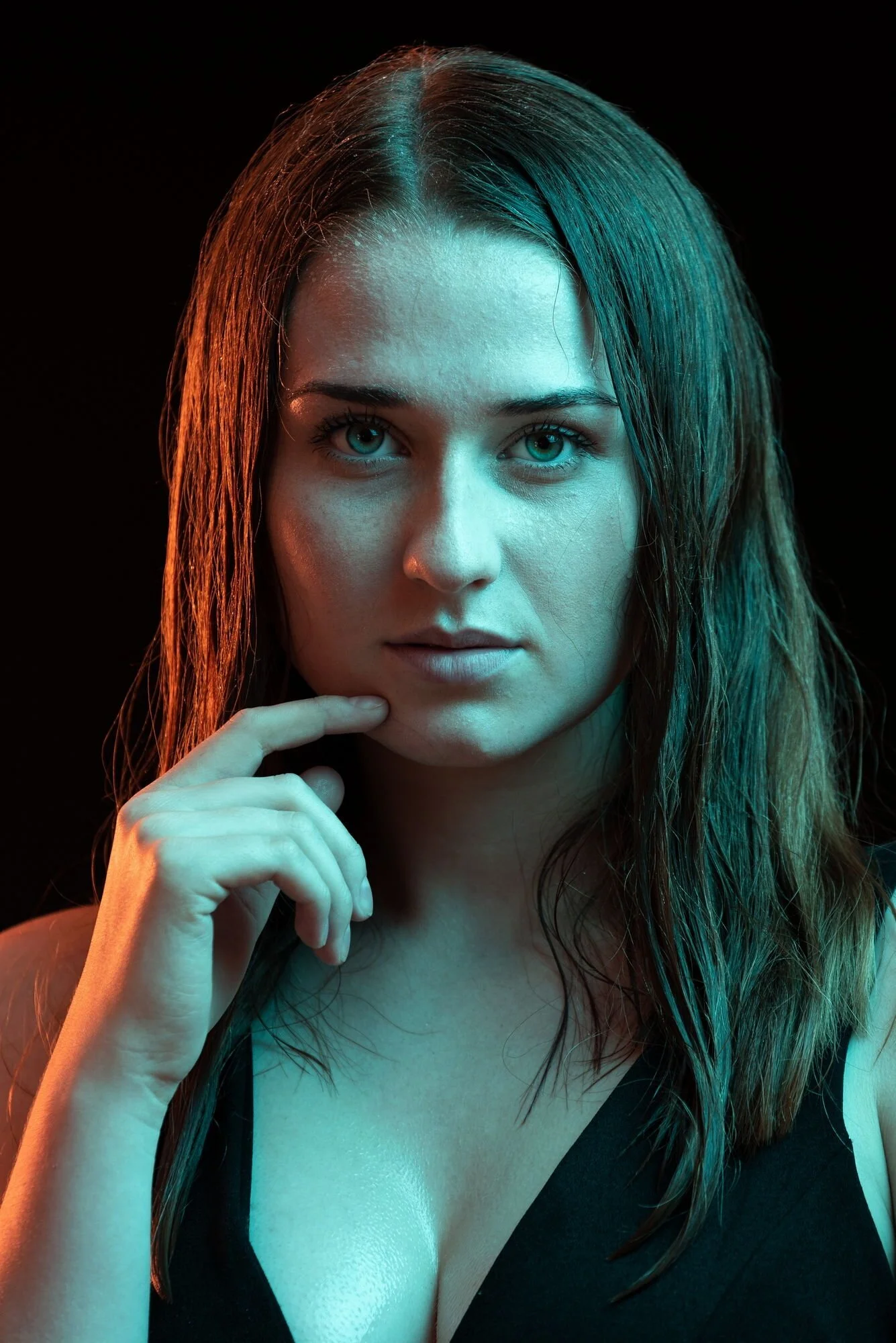 Porträt einer jungen Frau mit nassen Haaren, schwarz Kleid, blickt ernst in die Kamera, dunkler Hintergrund, farbige Beleuchtung