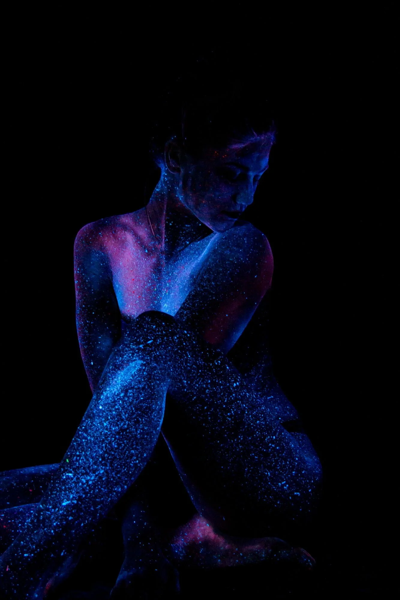 Frau mit leuchtender, galaxy-inspirierter Körperbemalung auf schwarzem Hintergrund.