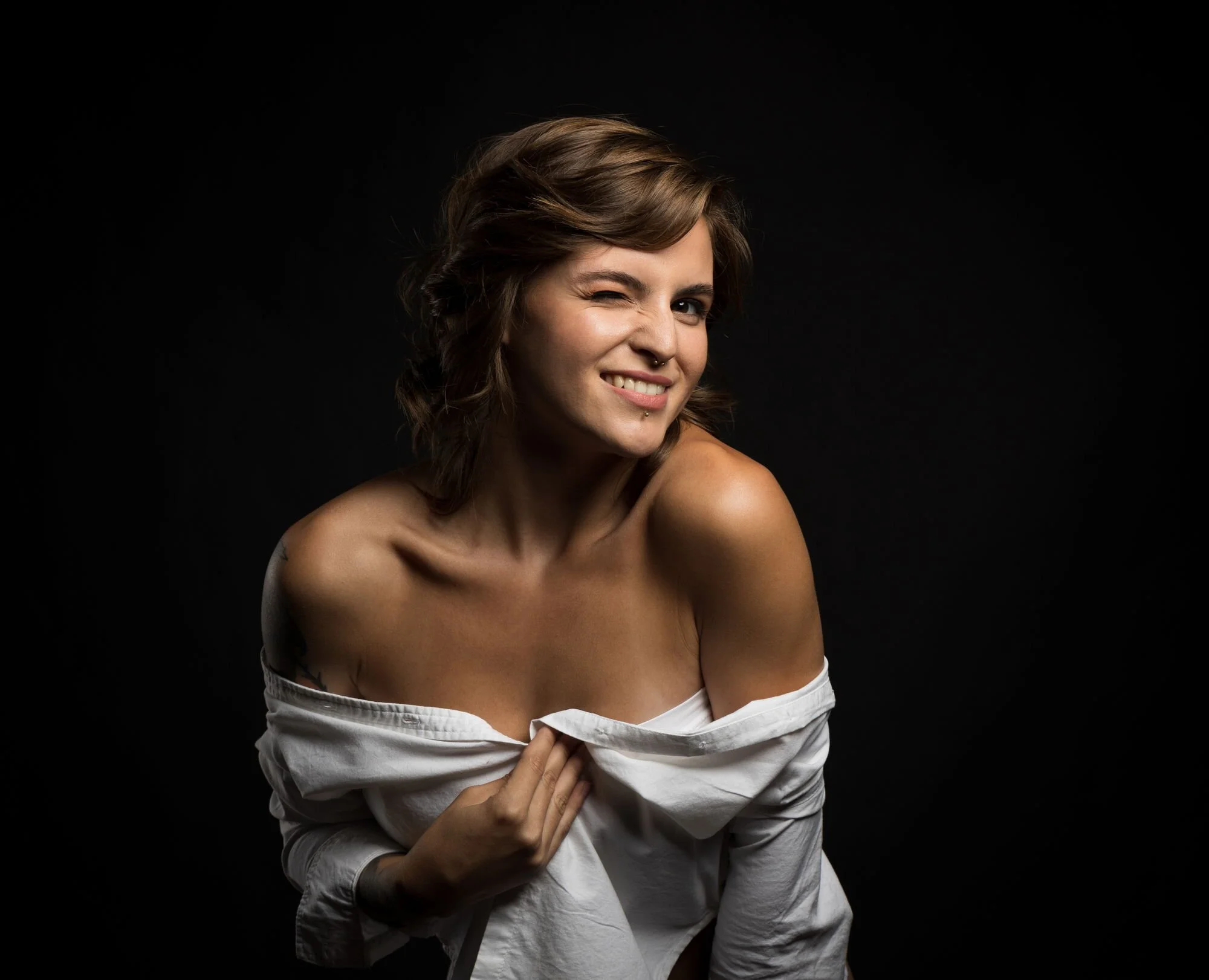 Junge Frau mit grüner Kleidung, die ein weißes Hemd trägt, lacht und zeigt den Mittelfinger, gegen schwarzen Hintergrund.