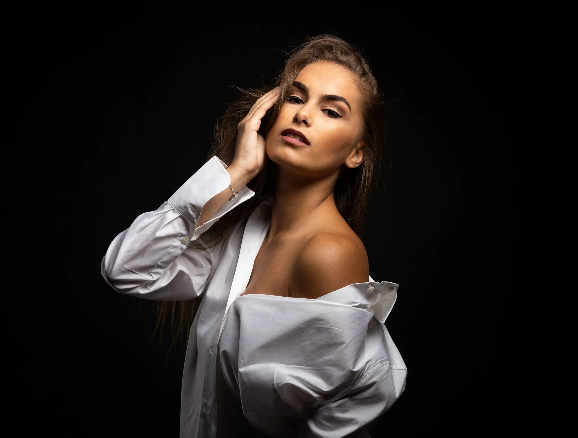 Junge Frau mit off shoulder weißen Hemd vor schwarzem Hintergrund