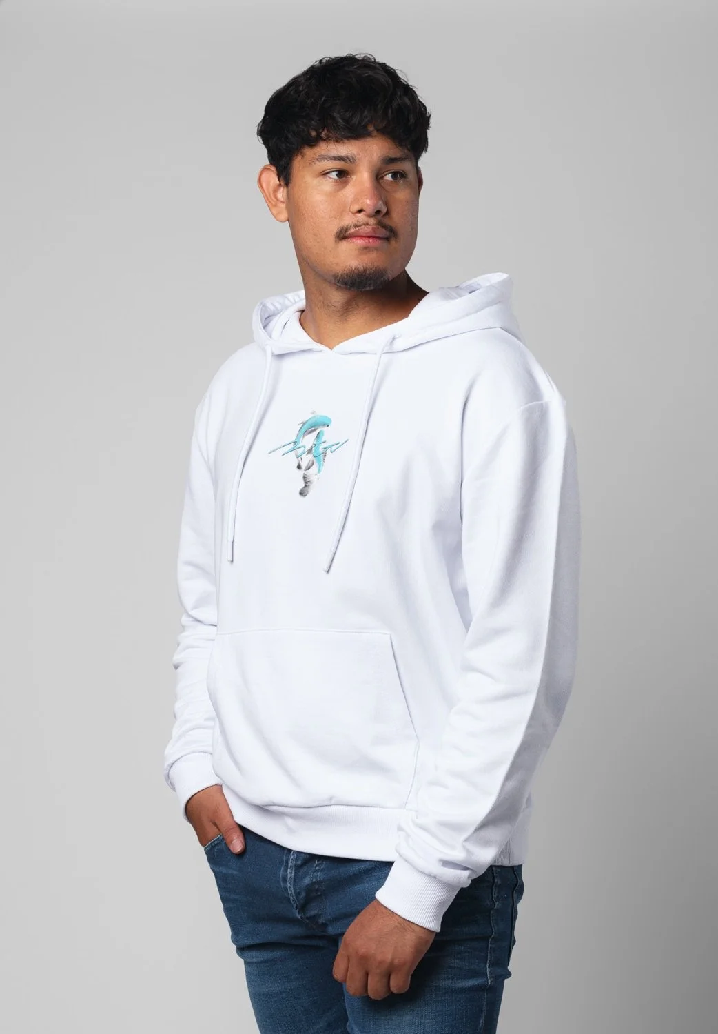 Junger Mann trägt weißen Hoodie mit Delfin-Design, steht vor grauem Hintergrund.
