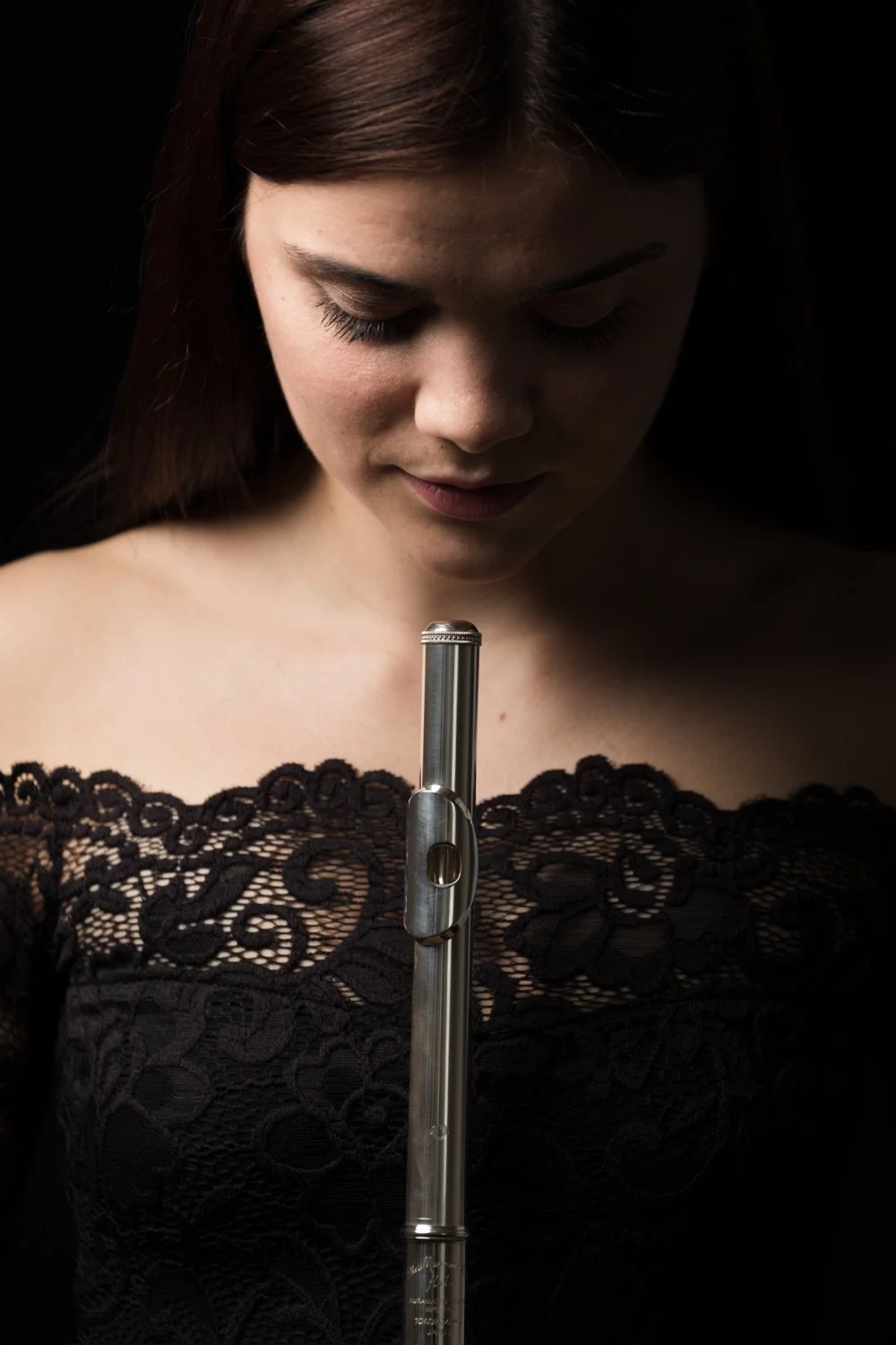 Junge Frau in schwarzem Spitzenkleid schaut auf eine Flöte gegen den dunklen Hintergrund.
