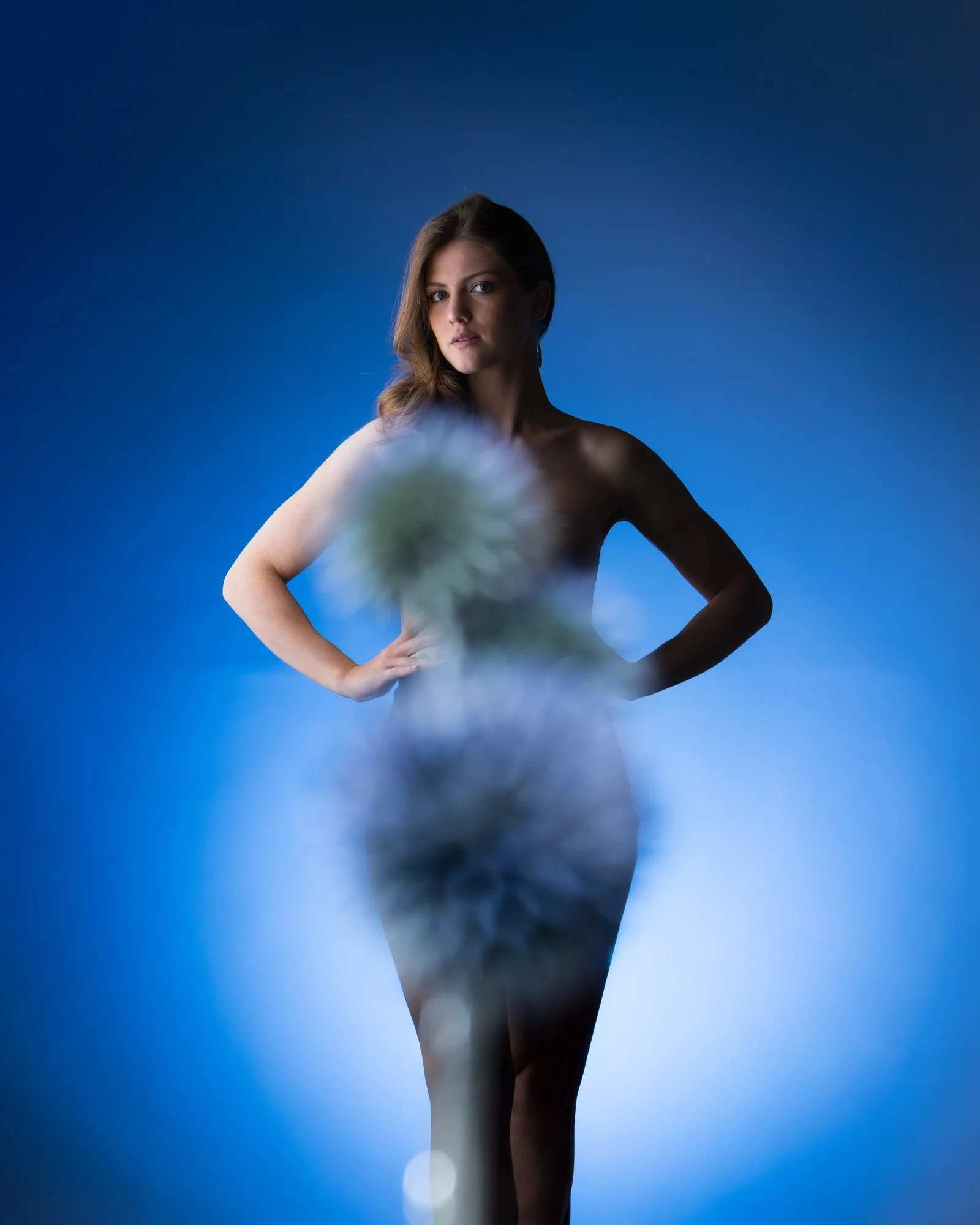 Frau steht vor einem blauen Hintergrund, blickt nach vorne, mit einem unscharfen Pflanze im Vordergrund