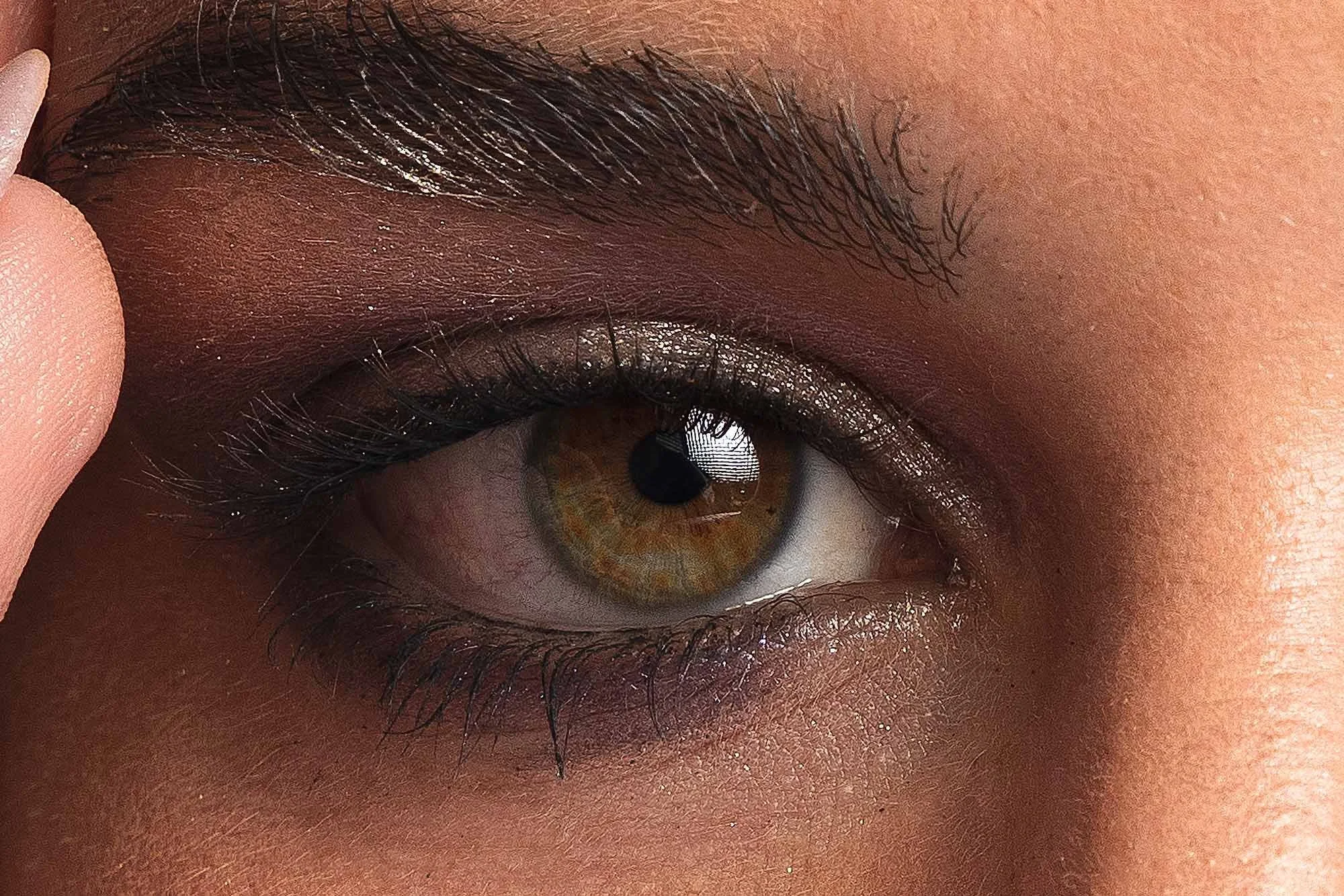 Nahaufnahme eines menschlichen Auges mit brauner Iris und schwarzen Wimpern, reflektiert im Auge ein Licht und ein Fenster.