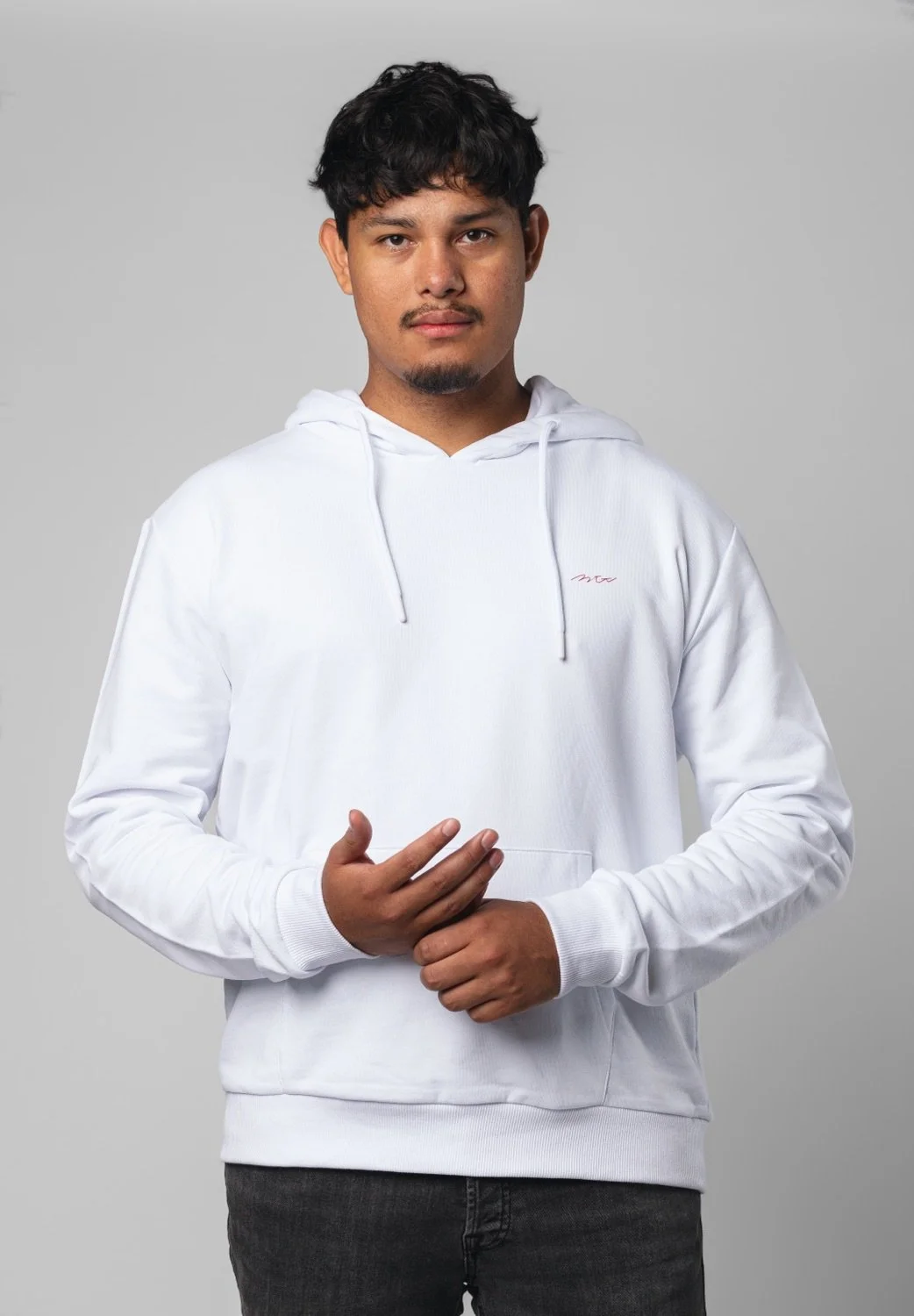 Ein junger Mann in einem weißen Hoodie steht vor einem grauen Hintergrund.