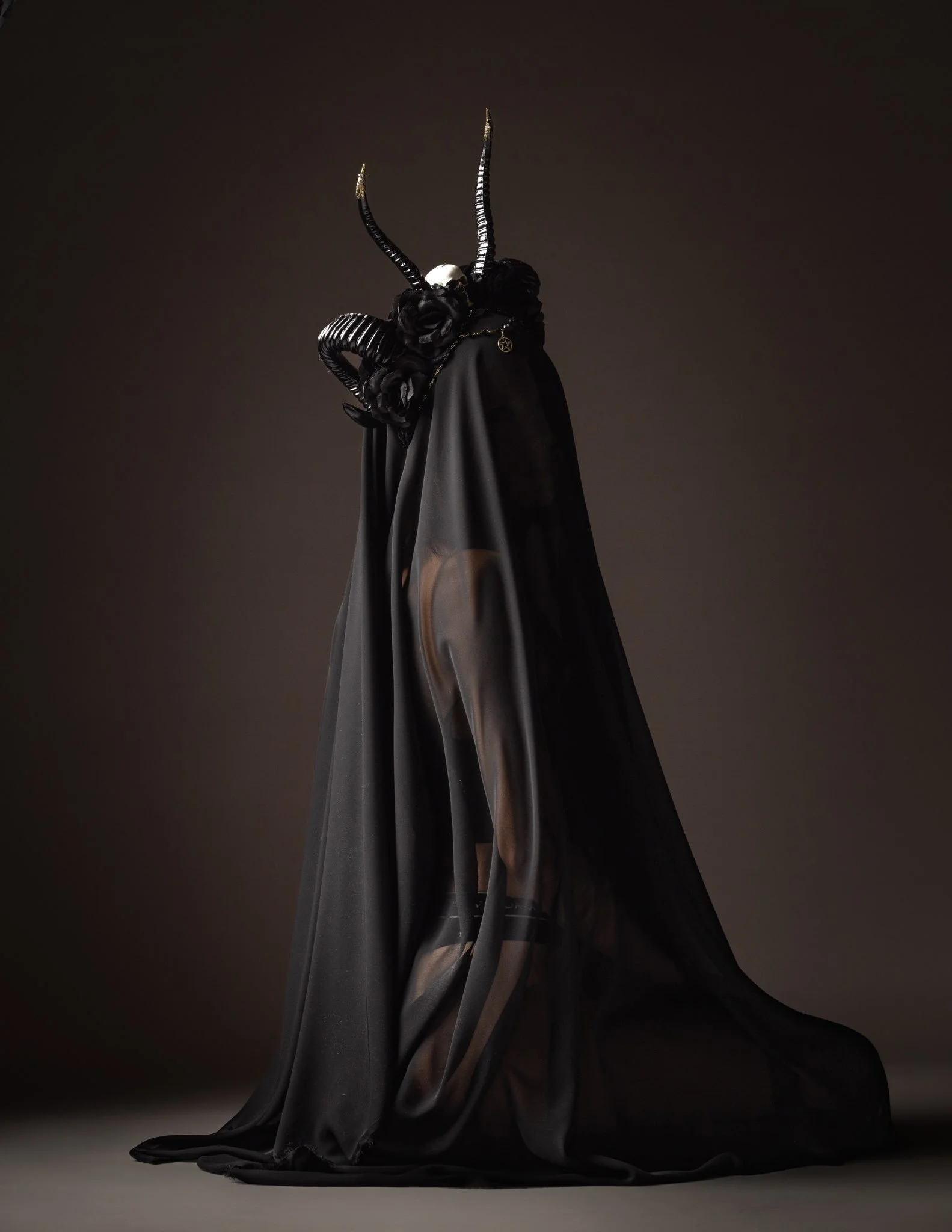 Skulptur eines mysteriösen Wesens mit langen, gekrümmten Hörnern, schwarze Blüten und einer schwarzen, glatten Jacke, die eine menschliche Figur verhüllt.