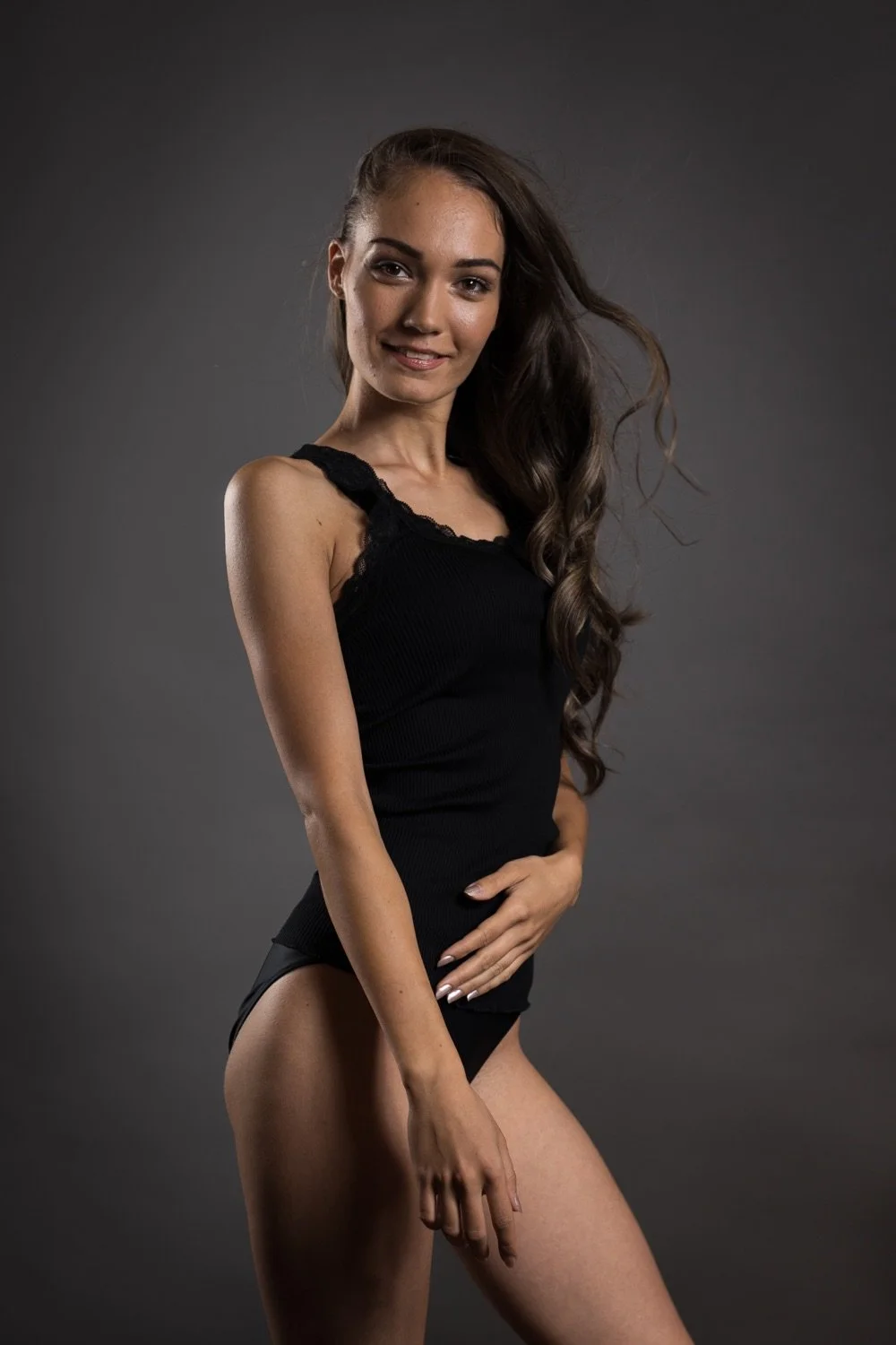 Junge Frau in schwarzem Oberteil und Unterwäsche posiert vor grauem Hintergrund.