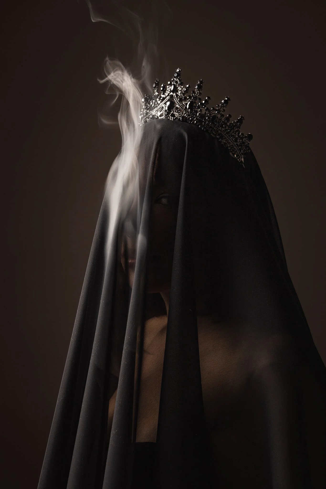 Eine dunkle, mystische Figur mit einem schwarzen Schleier, eine Krone und Rauch umgibt sie.