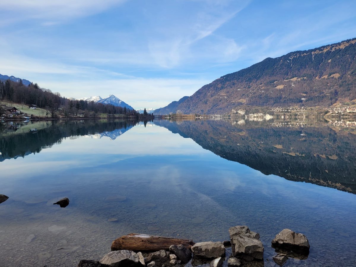 Blick auf einen ruhigen See mit Bergketten im Hintergrund, reflektiert im Wasser, bei klarer Wetterlage.