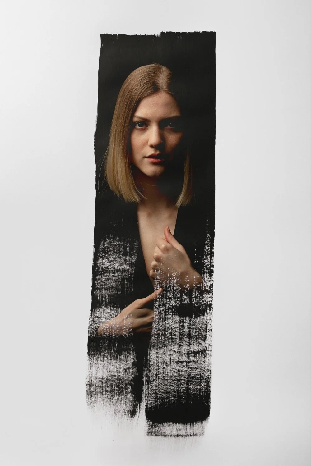 Porträt einer jungen Frau mit glatter, schulterlanger brauner Haarfrisur, Blick direkt in die Kamera, schwarze Kleidung vor einem schwarzen Hintergrund, teilweise durch eine zerbrochene, getrübte Glasscheibe sichtbar.