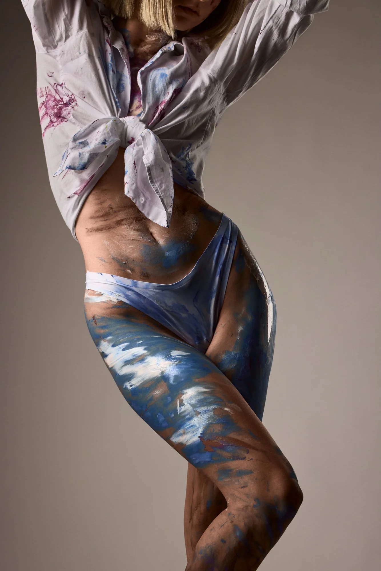 Frau mit bemalter Haut in provokanter Pose, trägt nur bunte Unterwäsche und ein Shirts, das an den Ärmeln geknotet ist.