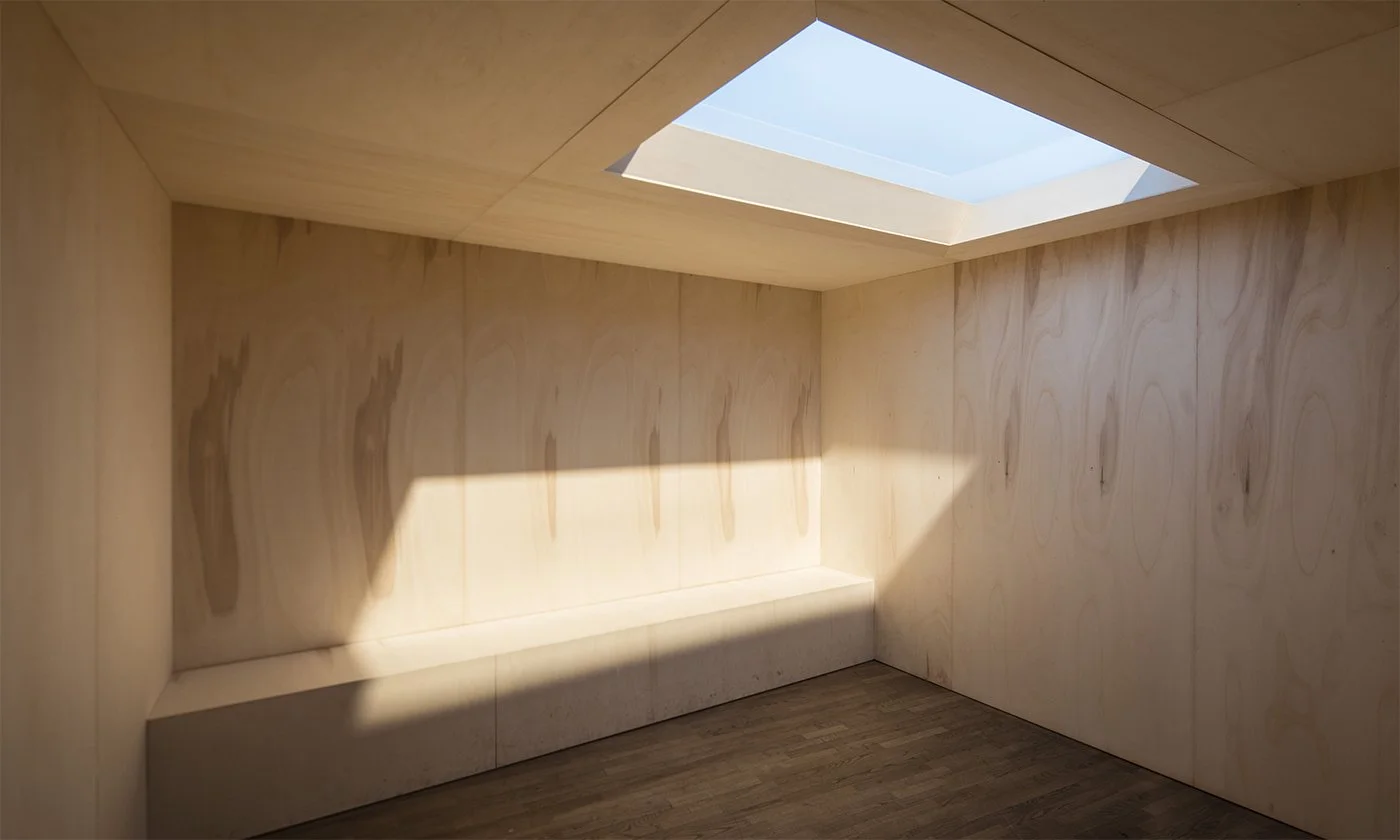A minimalist room with light wood paneling, a built-in bench, and a skylight that allows natural light to illuminate the space.