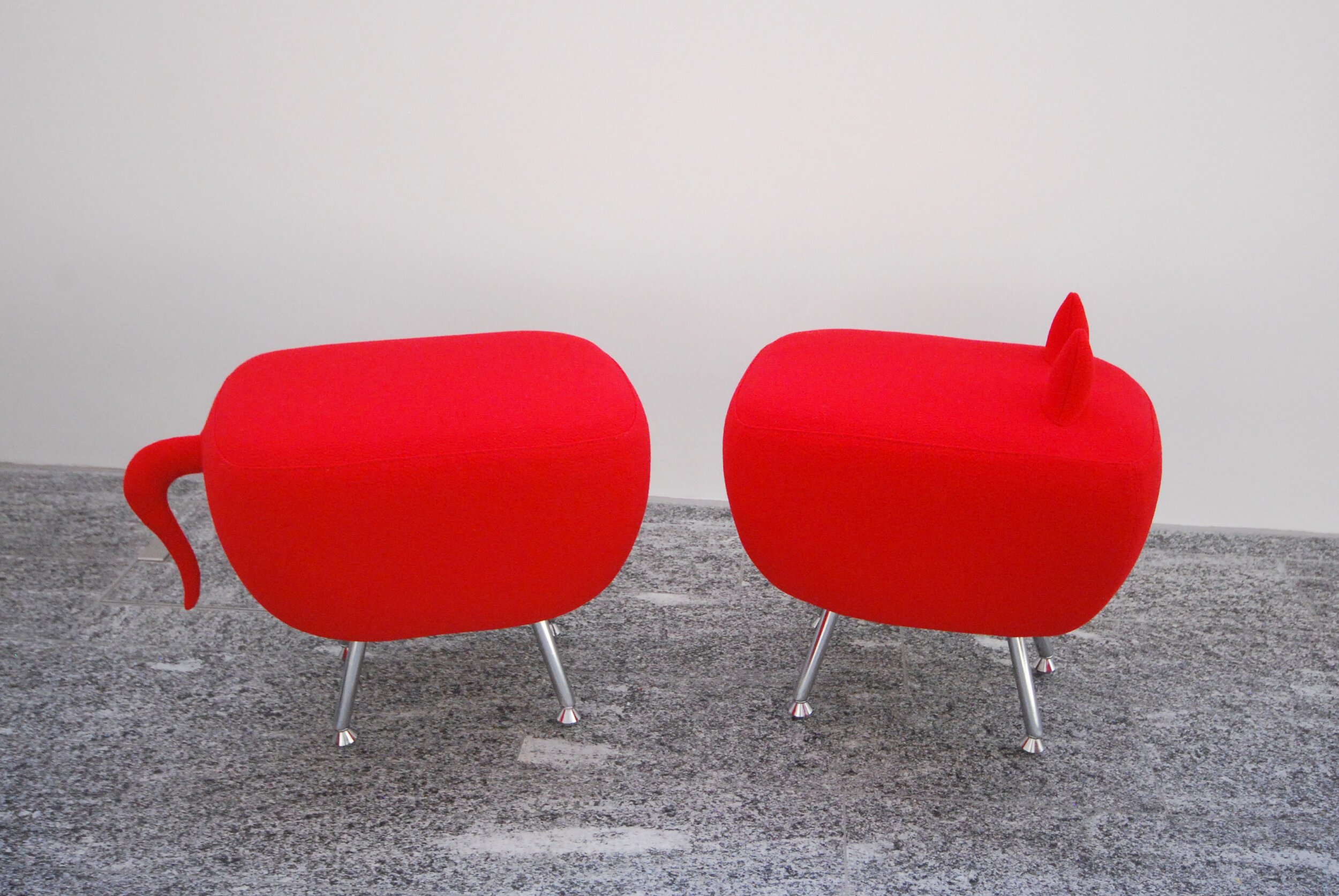 Two red animal-shaped stools with metal legs on a gray textured floor.