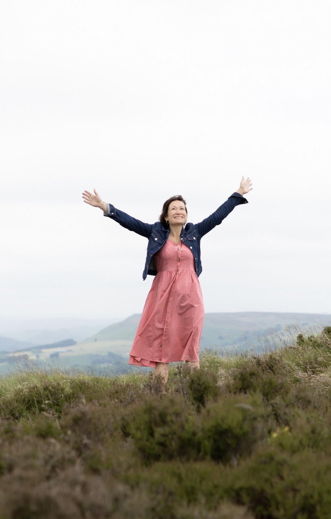 Women smiling with her arms in the air looking up to the clouds with the countryside in the background