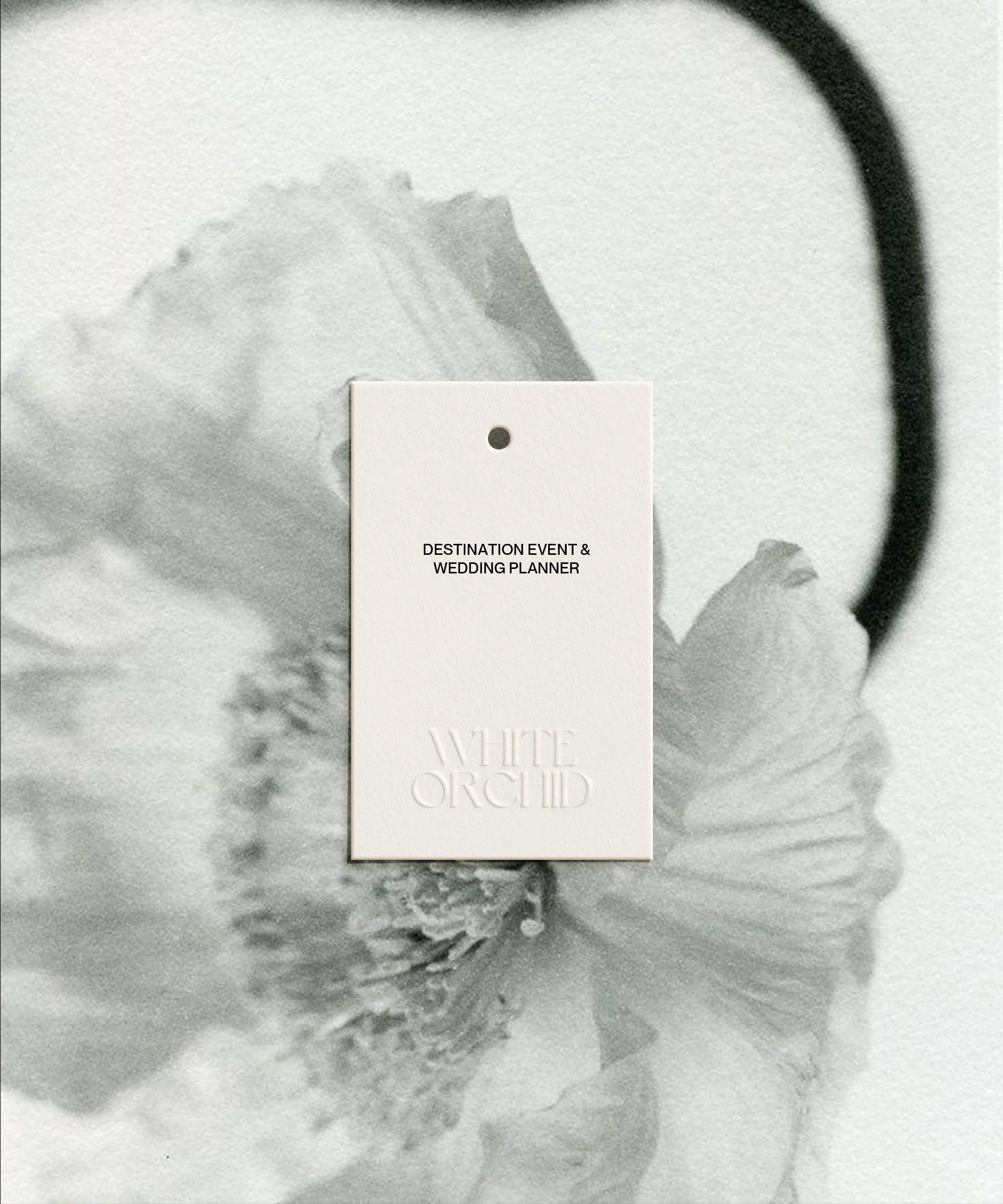 A grayscale image showing a close-up of a flower with a card labeled 'Destination Event & Wedding Planner White Orchid.' The card is placed over the flower's center.