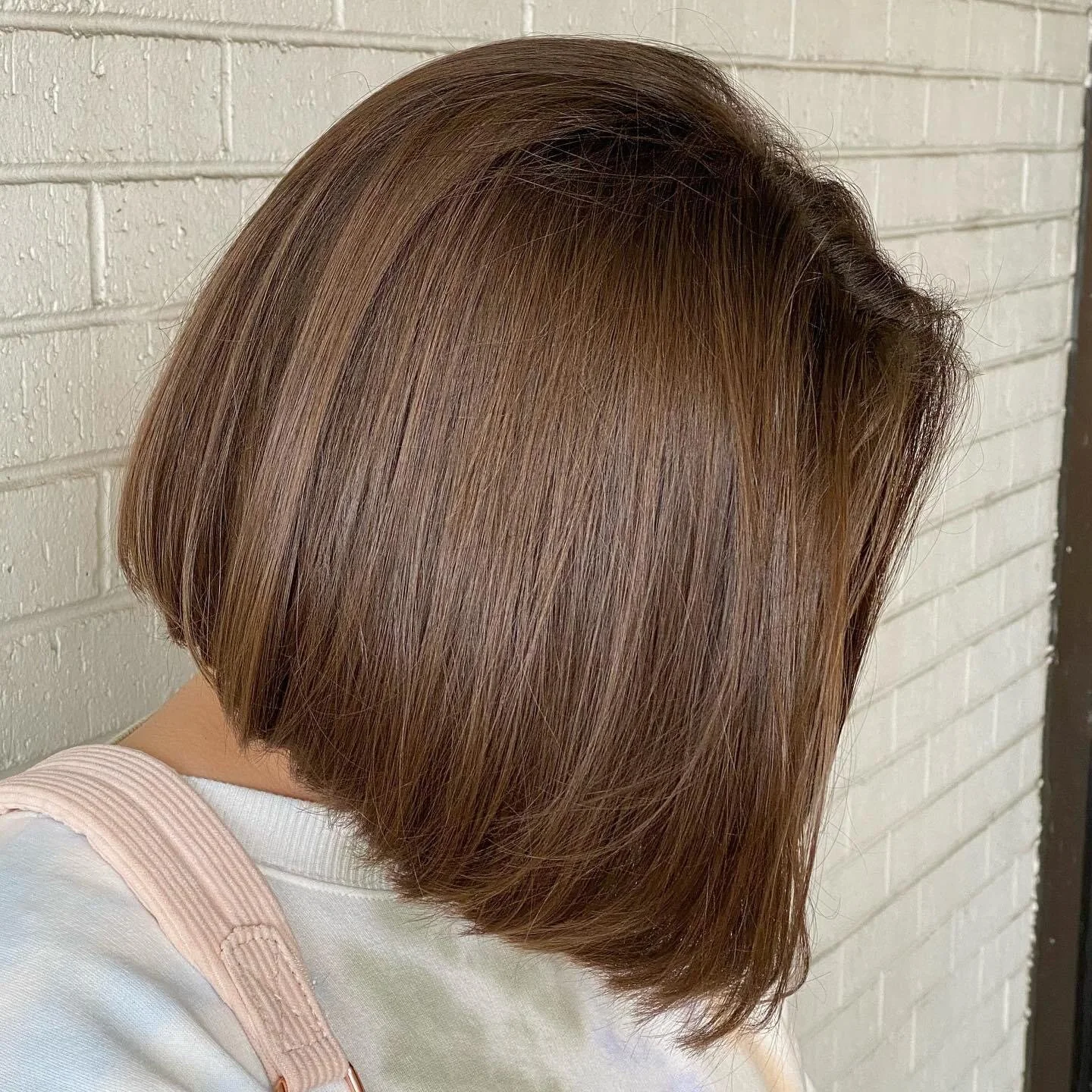 Person with a brown bob hairstyle facing a white brick wall.