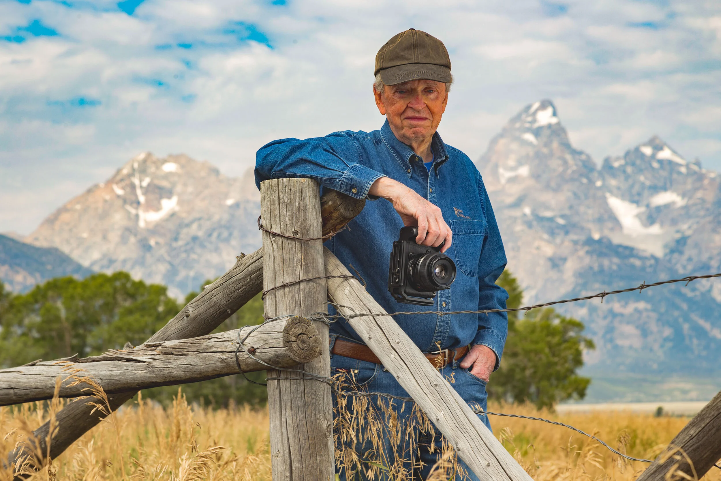 Photographer leaning on a ranch fence with the Tetons behind