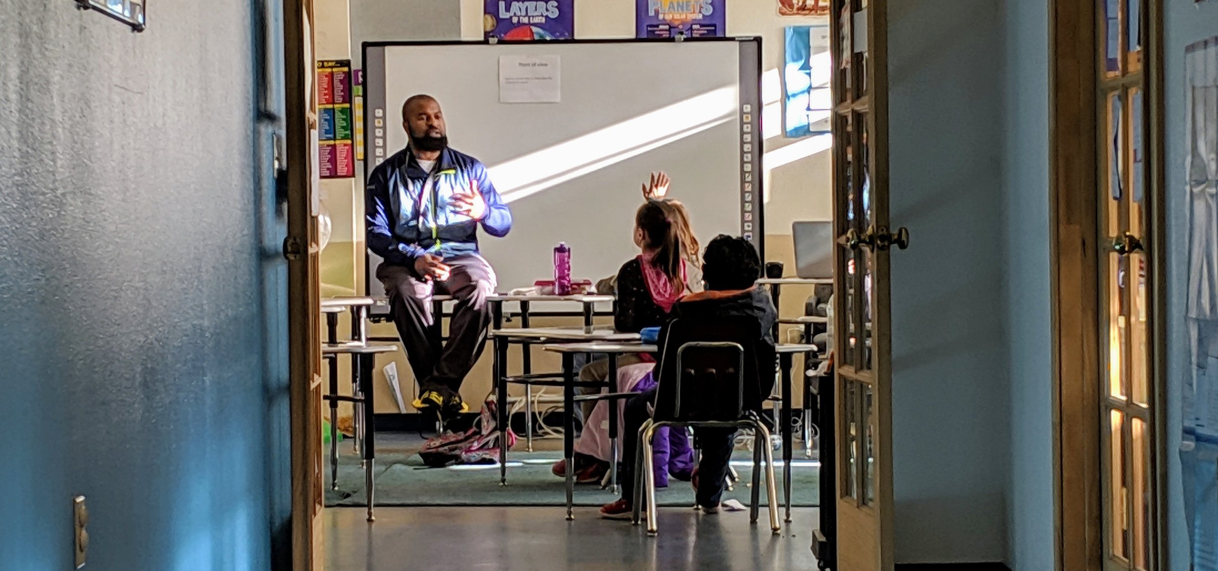 Young-African-American-male-sitting-on-table-teaching-in-a-classroom.jpg