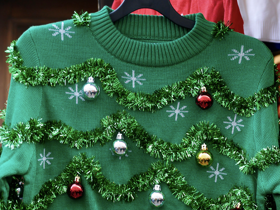 Green Christmas sweater decorated with tinsel, small ornaments, and snowflake patterns.