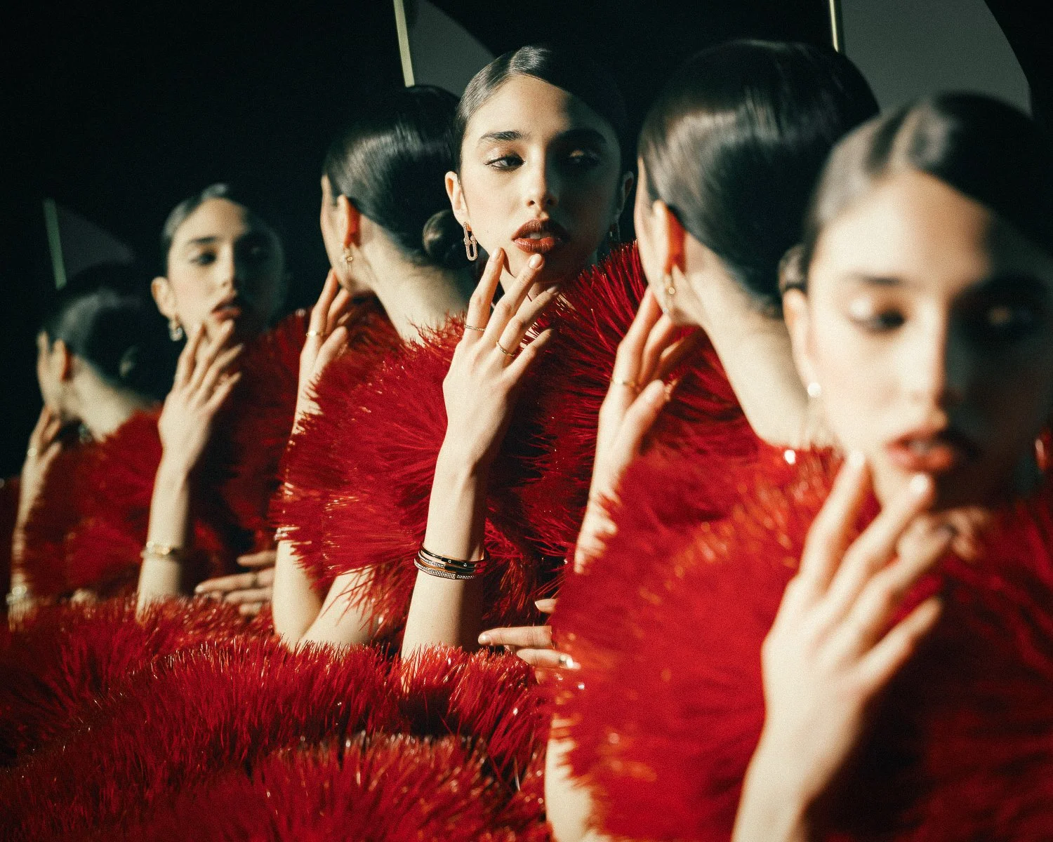 A woman in a red feathered dress looking at her reflection in a mirror with multiple reflections of herself surrounding her.