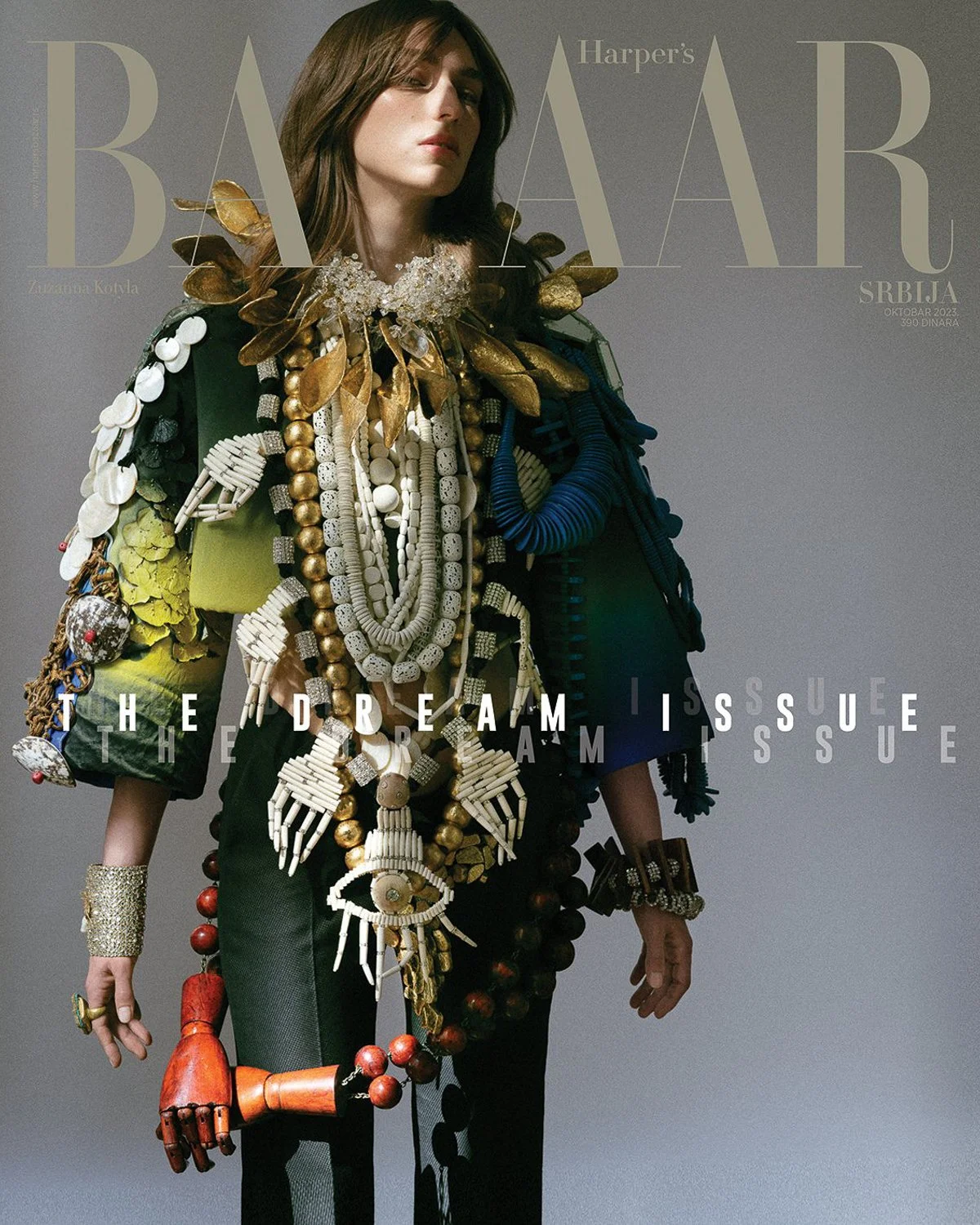 Fashion magazine cover featuring a woman with brown hair and an elaborate outfit decorated with necklaces, jewelry, and accessories, against a gray background with the text 'Harper's Bazaar' and magazine details.