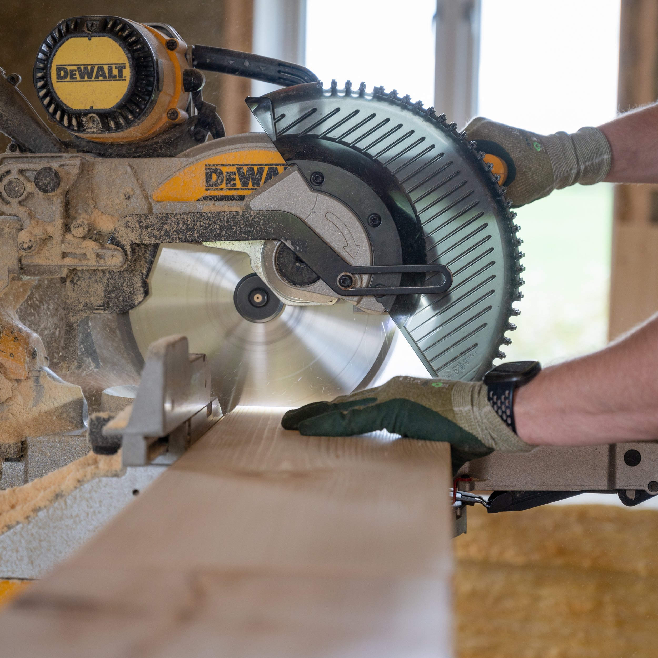 En person bruker en sirkelsag til å kutte gjennom ei trestokk. Sirkelsagen er elektrisk og merket DEWALT. Personen har på seg arbeidshansker.