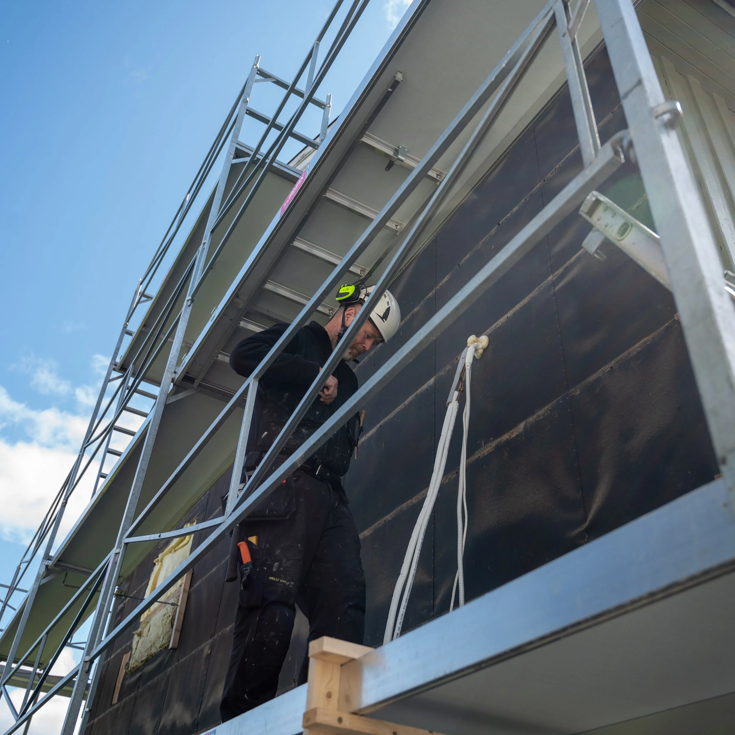 En mann i hjelm står på en byggeplattform og jobber med en bygning.