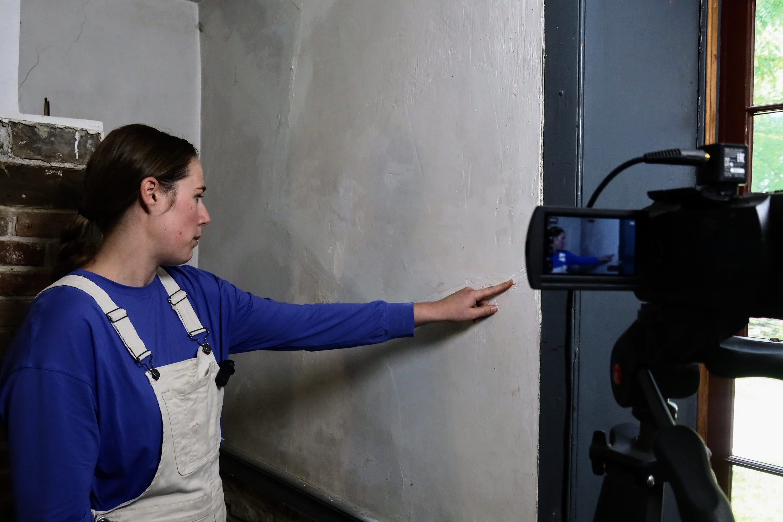 A heritage professional points at a plaster wall in a historic building to highlight what its markings might tell us. 