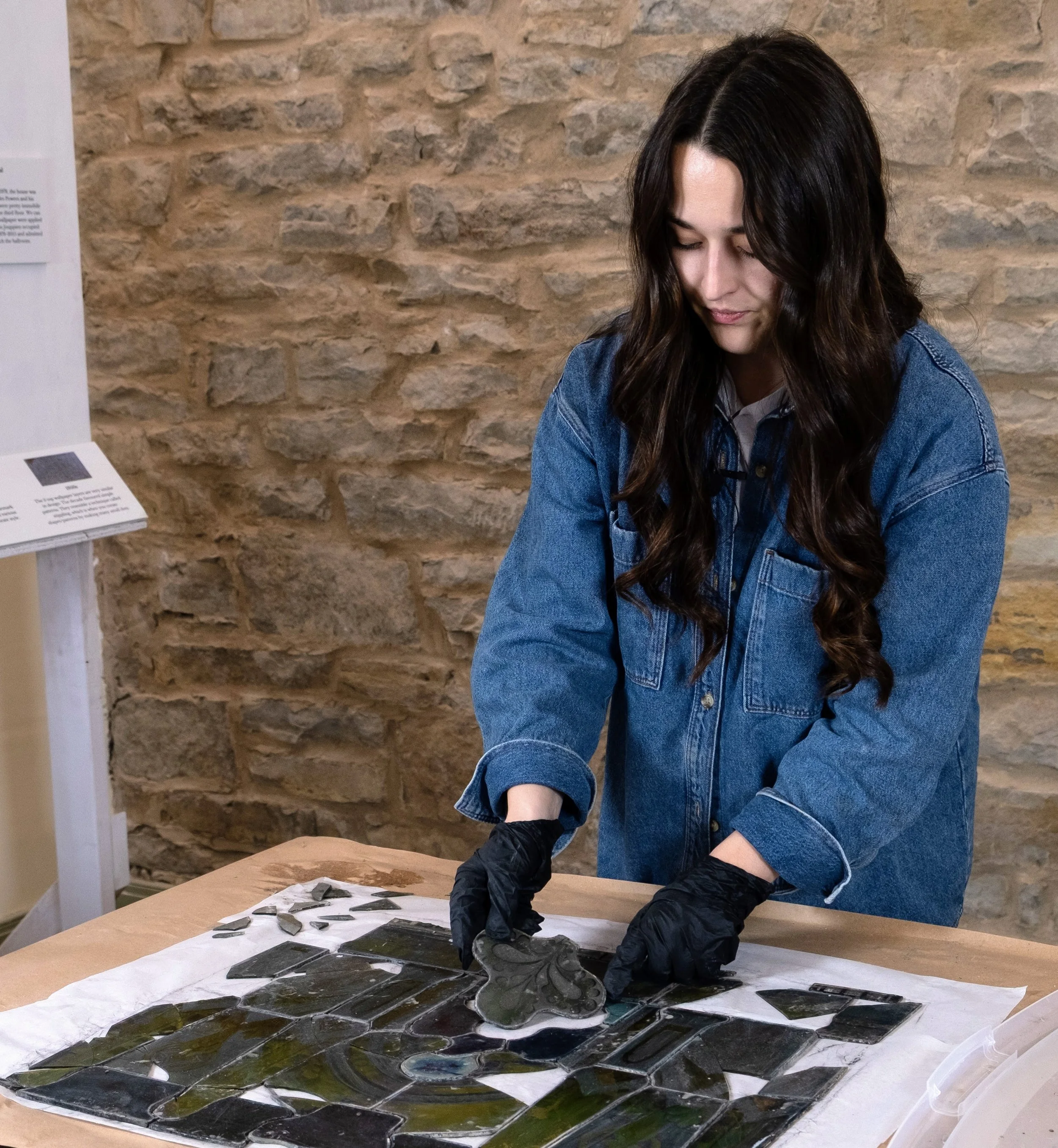 woman wears gloves as she handles disassembled glass pieces of a stained glass window.