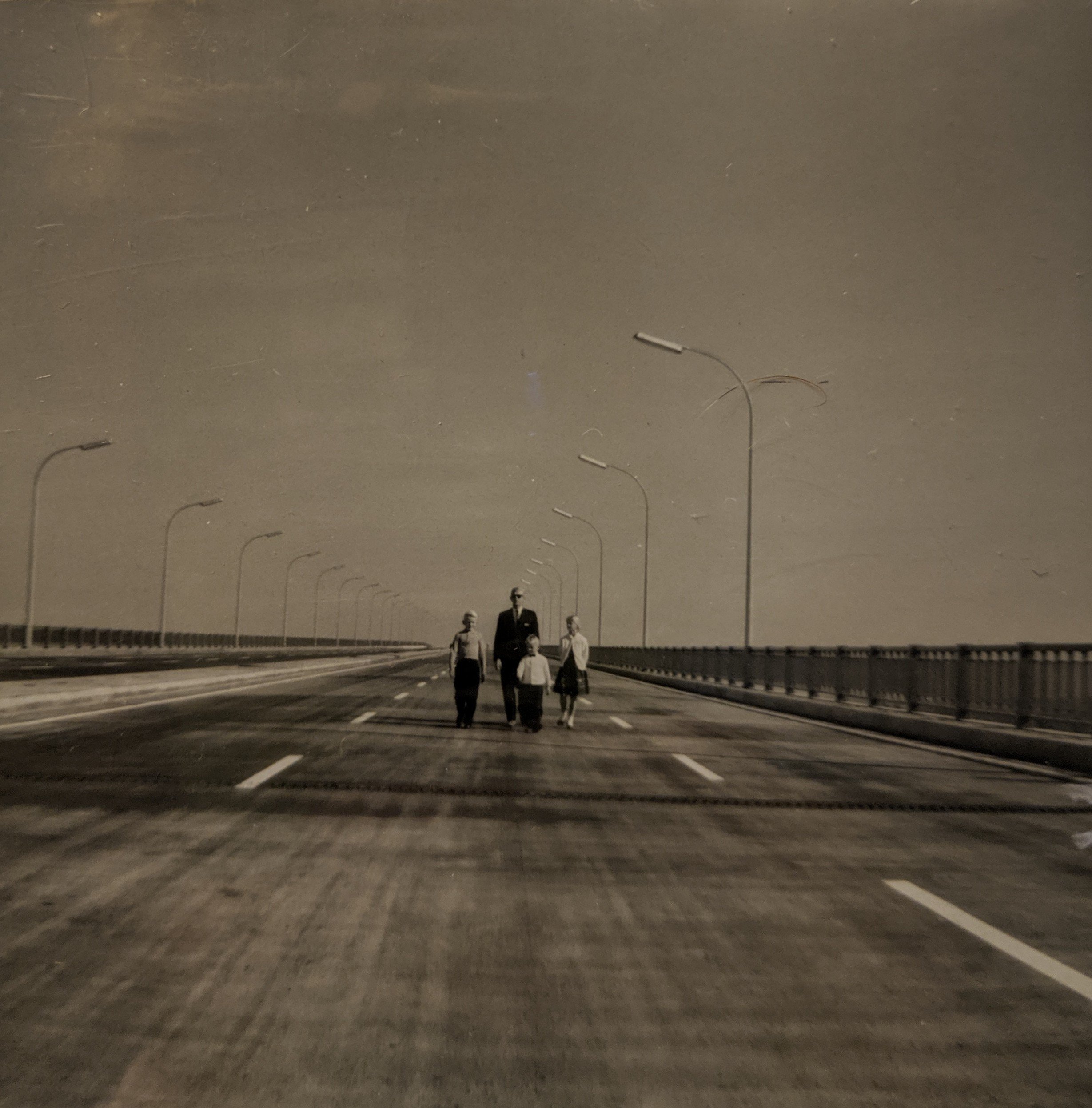 A father and three children stand in the middle of an empty highway.
