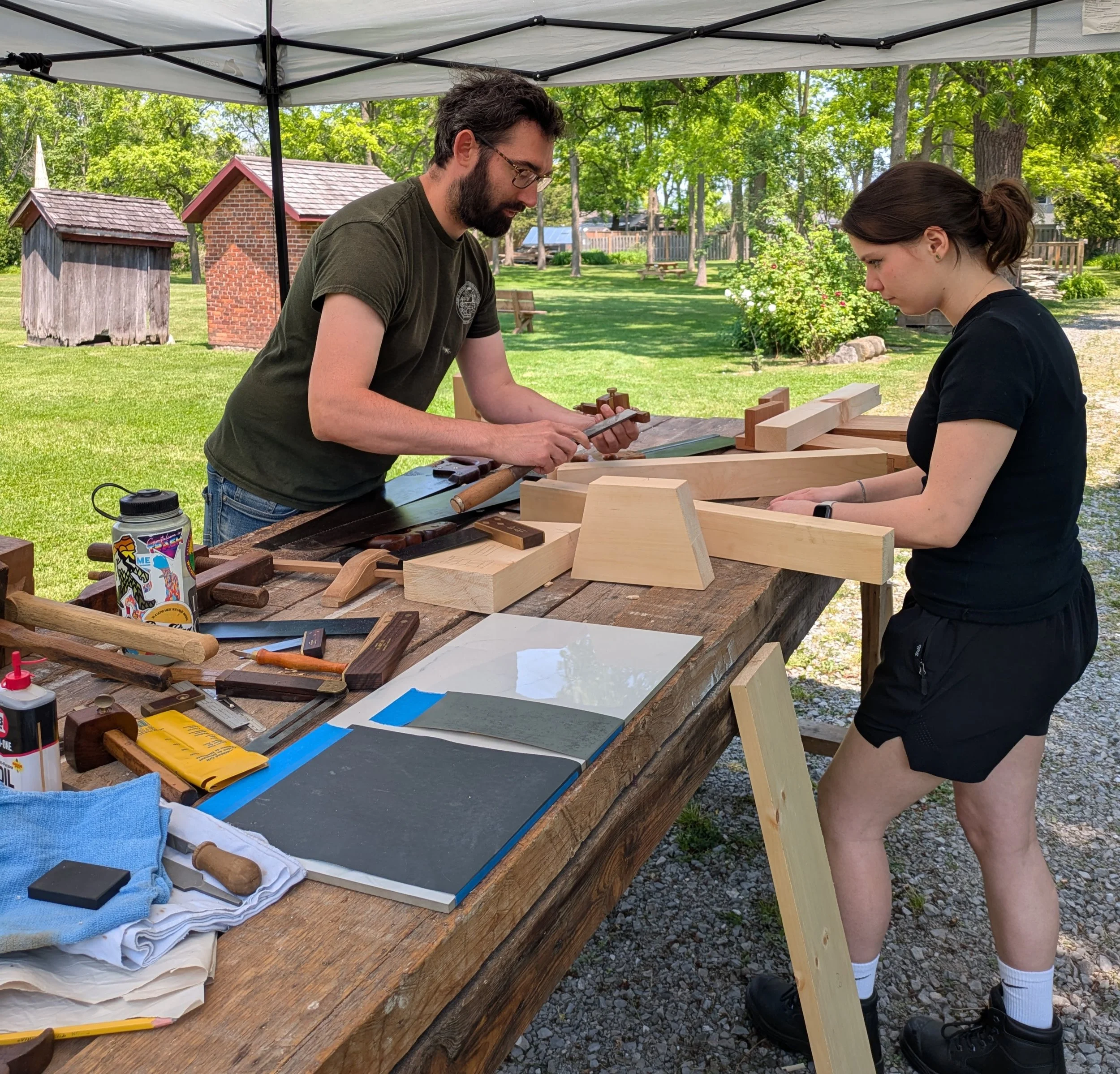 heritage wood worker demonstrates using traditional tools for visitor outside
