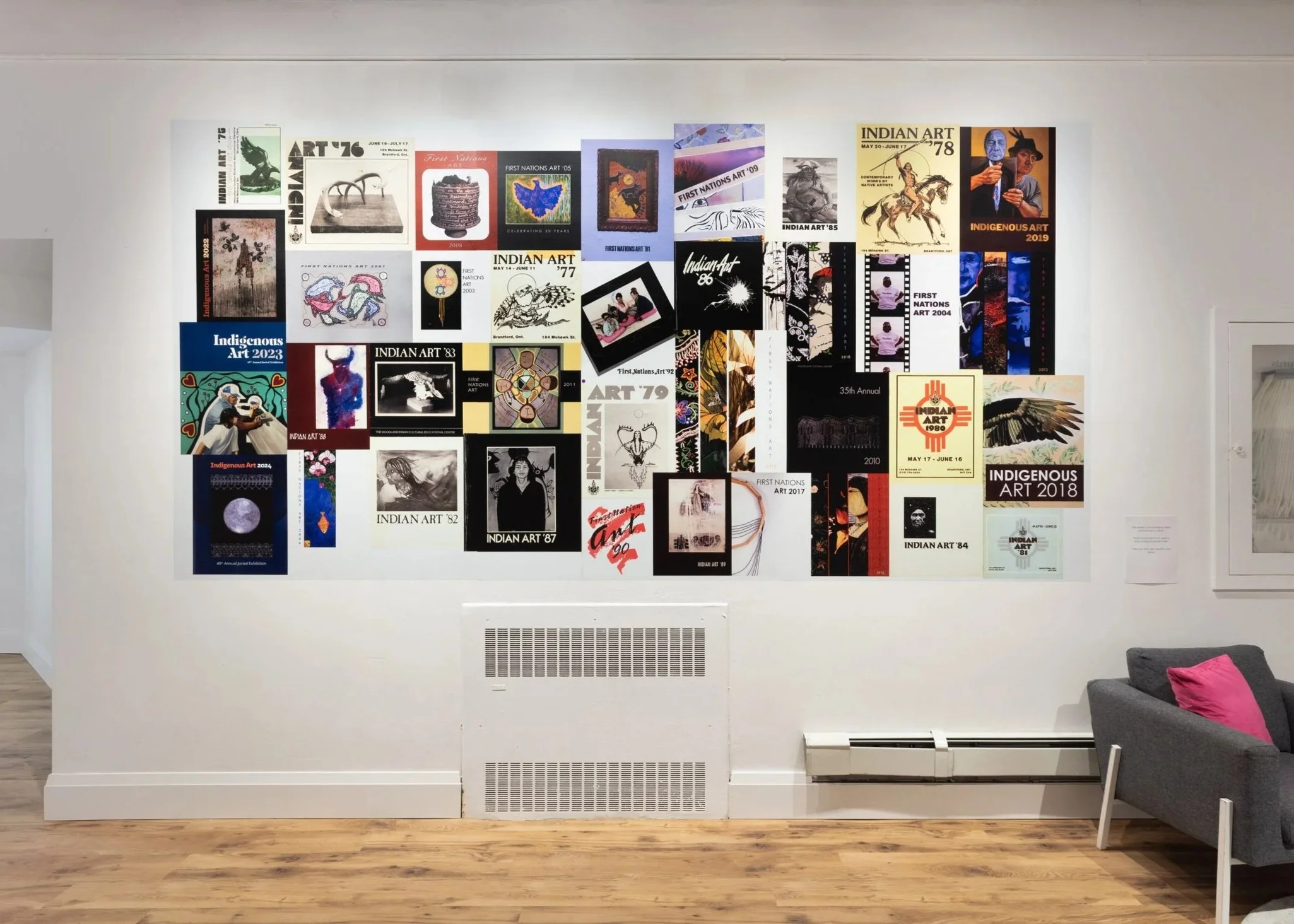 A series of colourful posters are poasted to a white wall. The posters are highly decorative and are meant to promote an arts exhibit.