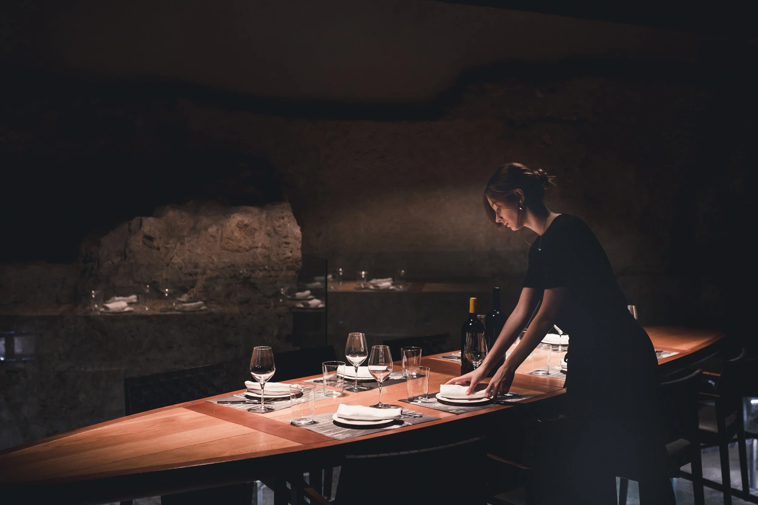 Une femme organise une table élégante dans un restaurant sombre avec un décor en roche.