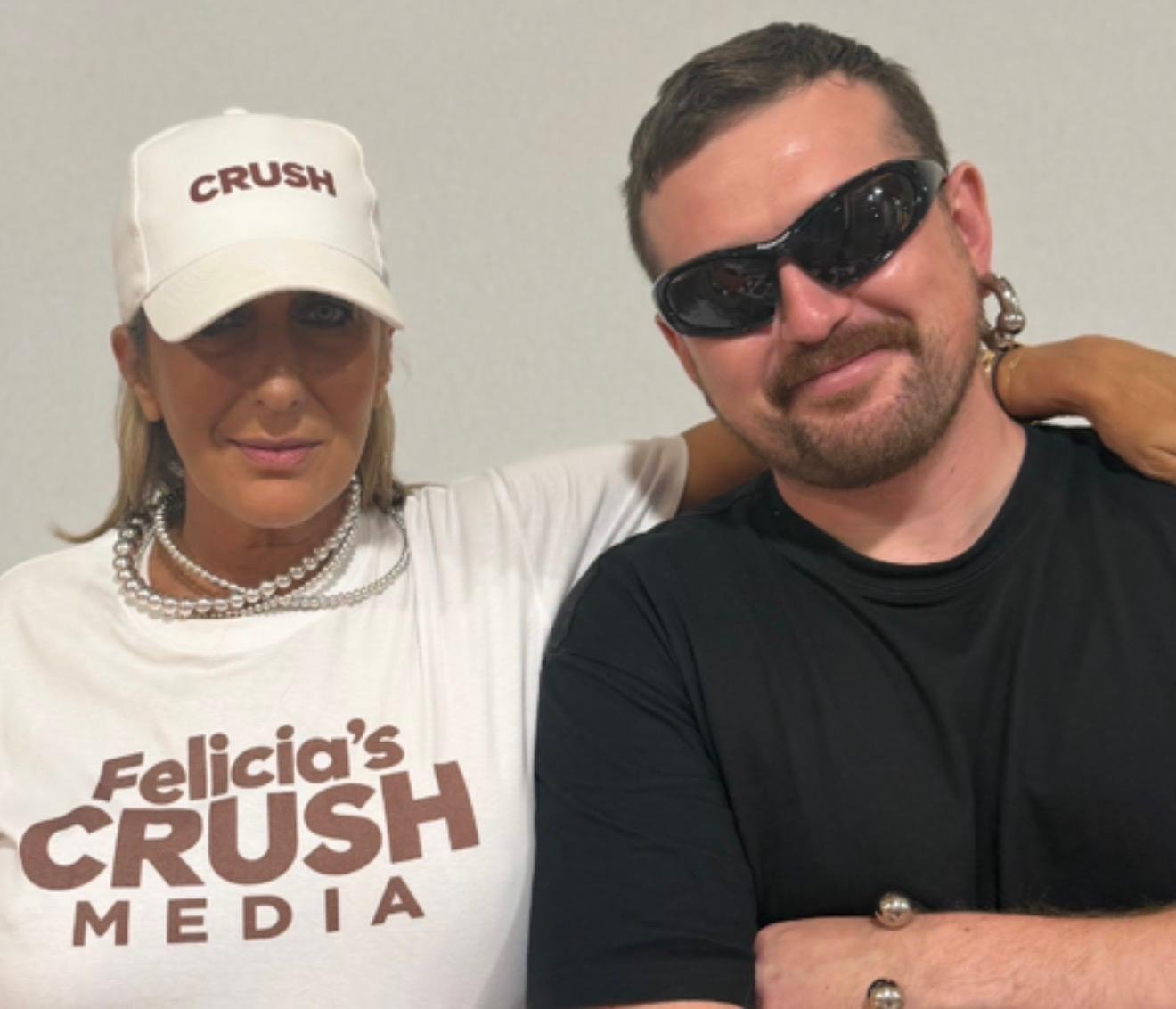 Deux personnes posent ensemble, une femme portant une casquette blanche avec 'CRUSH' inscrit, un t-shirt blanc, et une femme portant des lunettes de soleil noires, un t-shirt noir, avec une accolade sur l'épaule de l'autre personne.