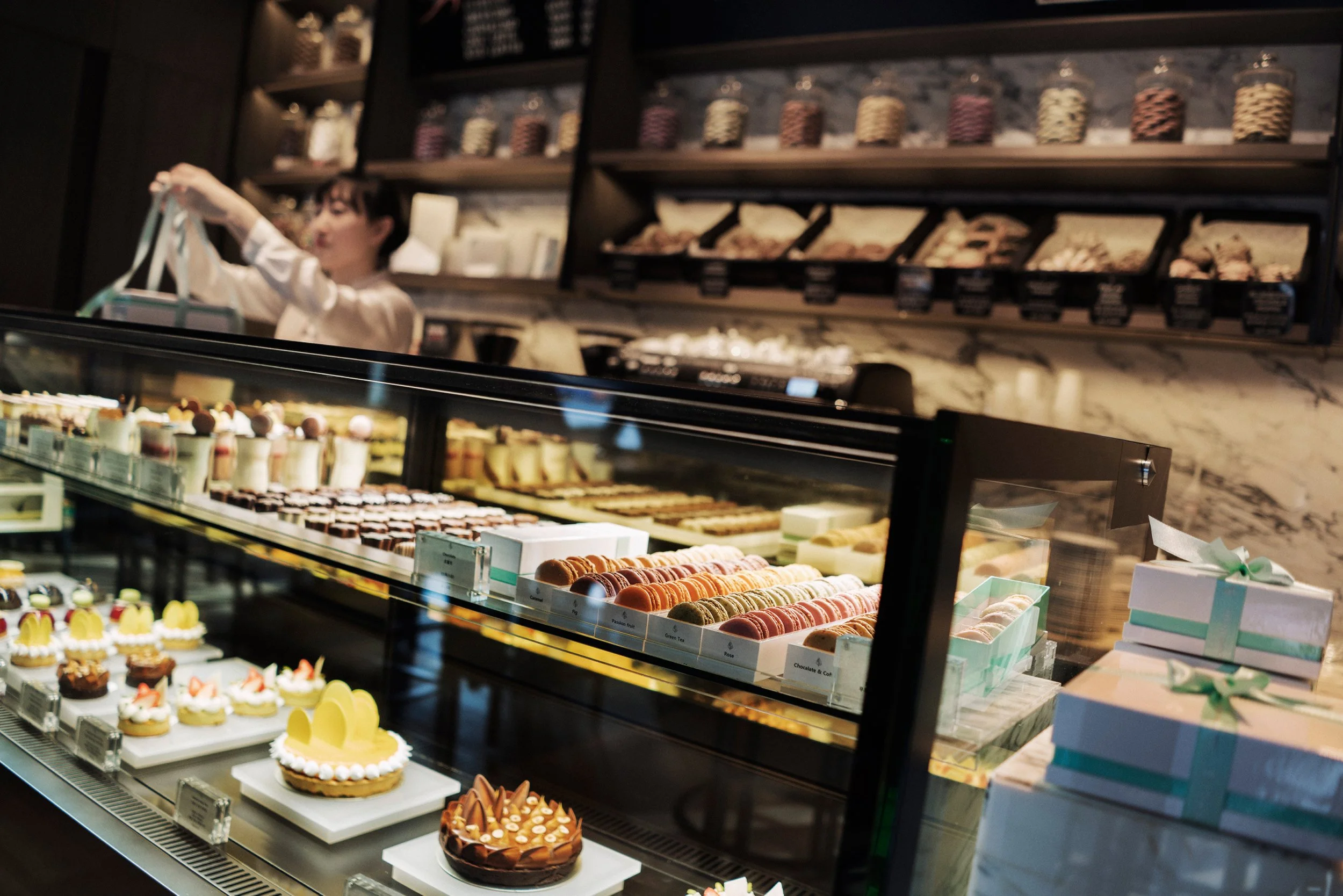 Vitrine de pâtisseries variées dans une pâtisserie moderne, avec une décoration élégante et des étagères de confiseries au fond.