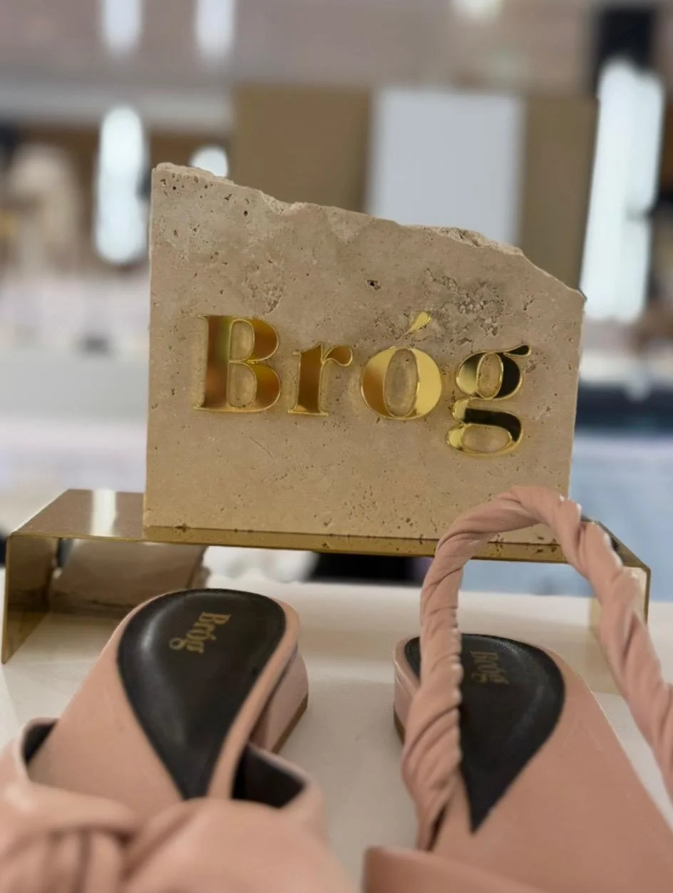 Une paire de chaussures roses posée devant un bloc de pierre avec le mot "Bru" écrit en lettres dorées, dans un environnement intérieur.